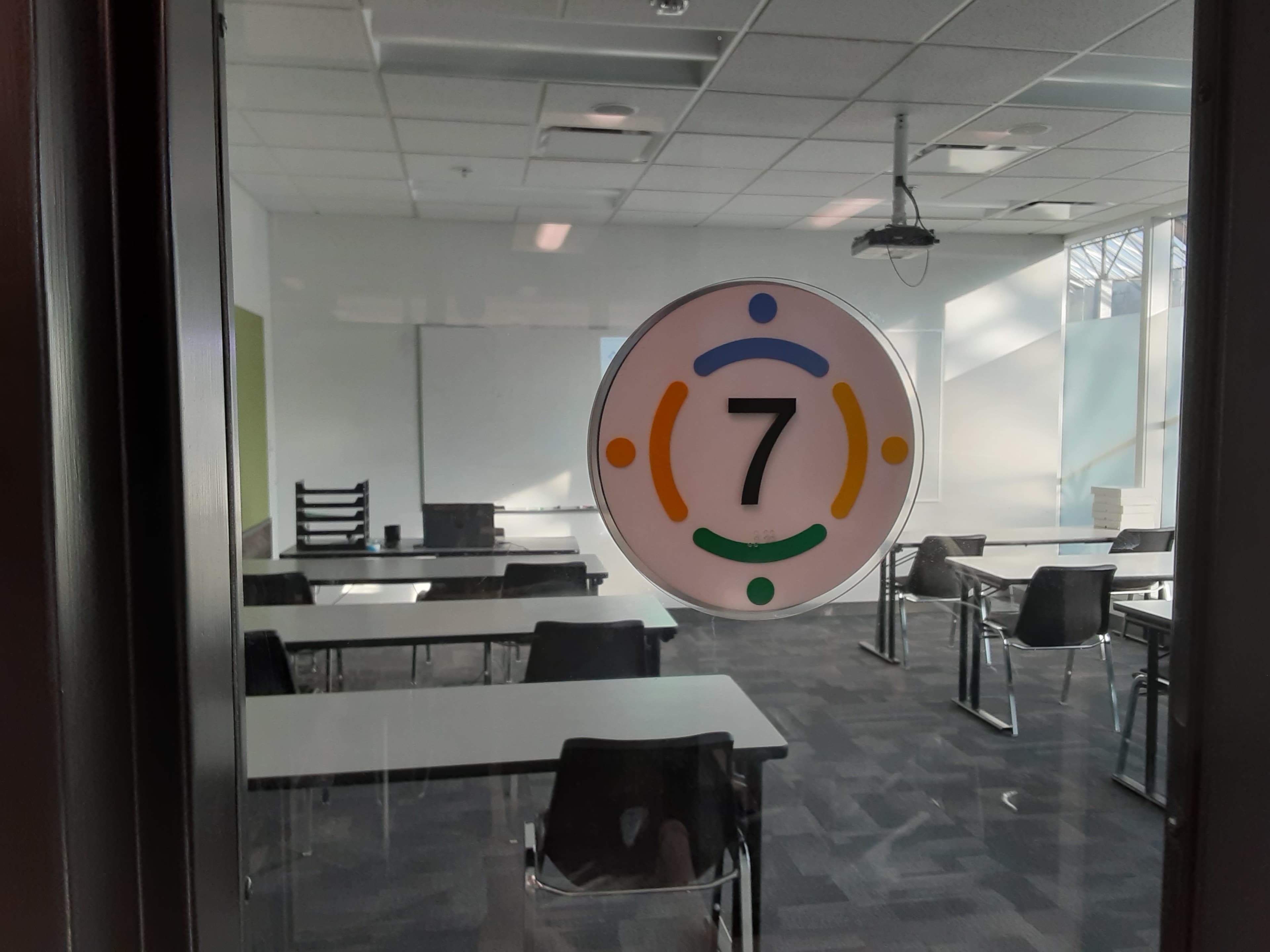A classroom door with a sign indicating "Room 7" and visible classroom furniture inside.