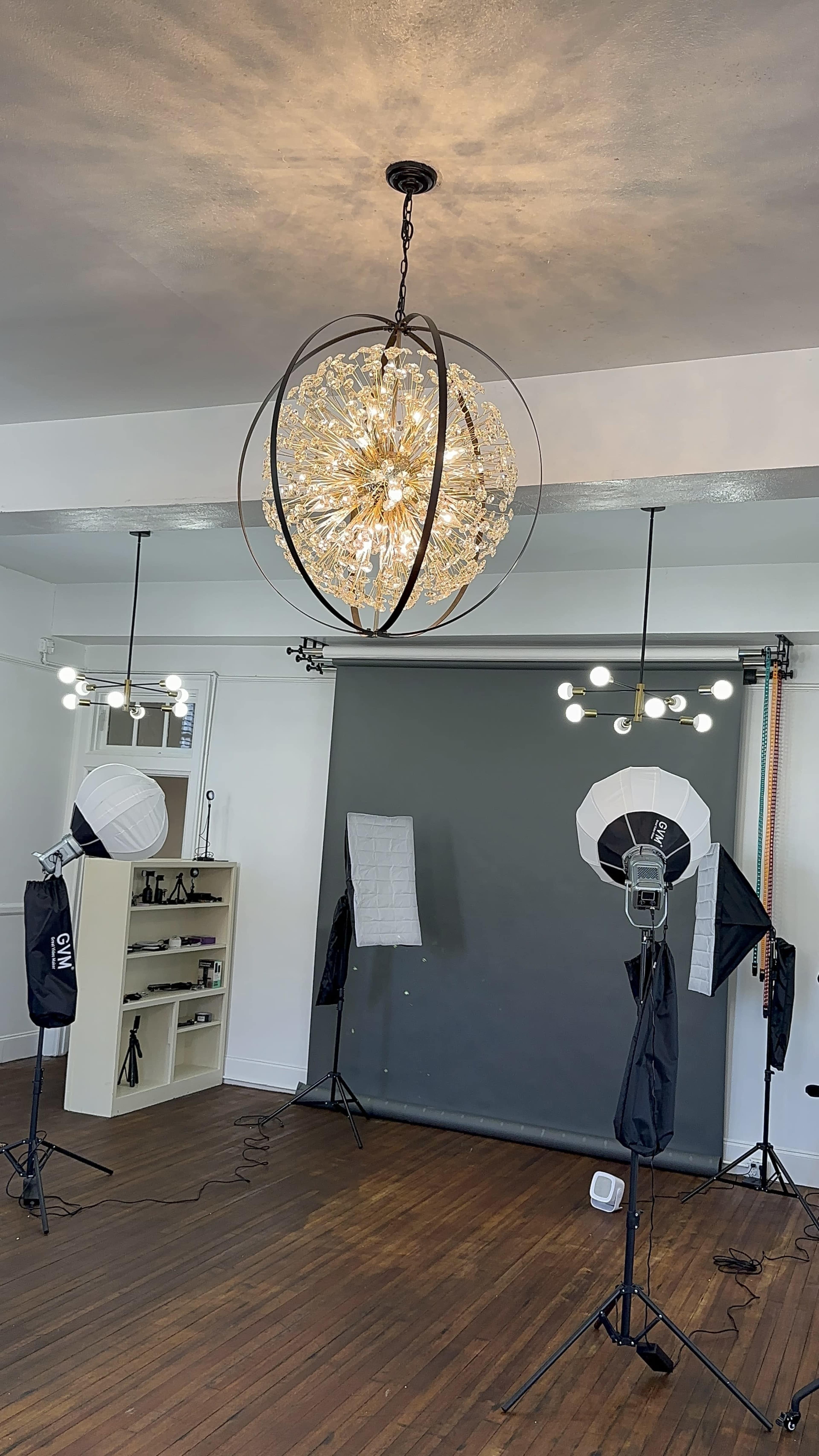 The image shows a photography studio with a decorative chandelier, two lighting setups, and a backdrop.