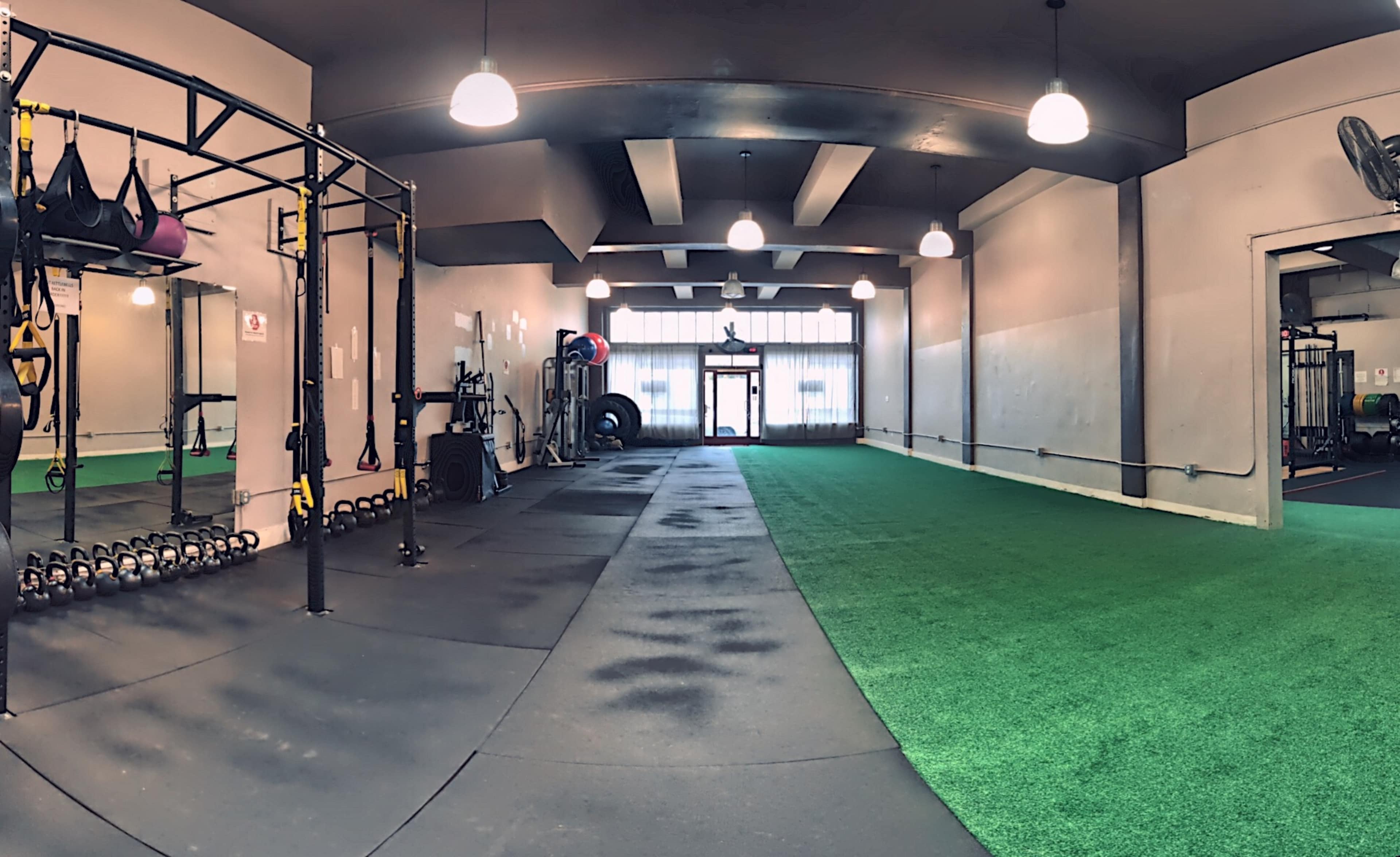 A spacious gym with rubber flooring, exercise equipment on one side, and a large window allowing natural light to enter.