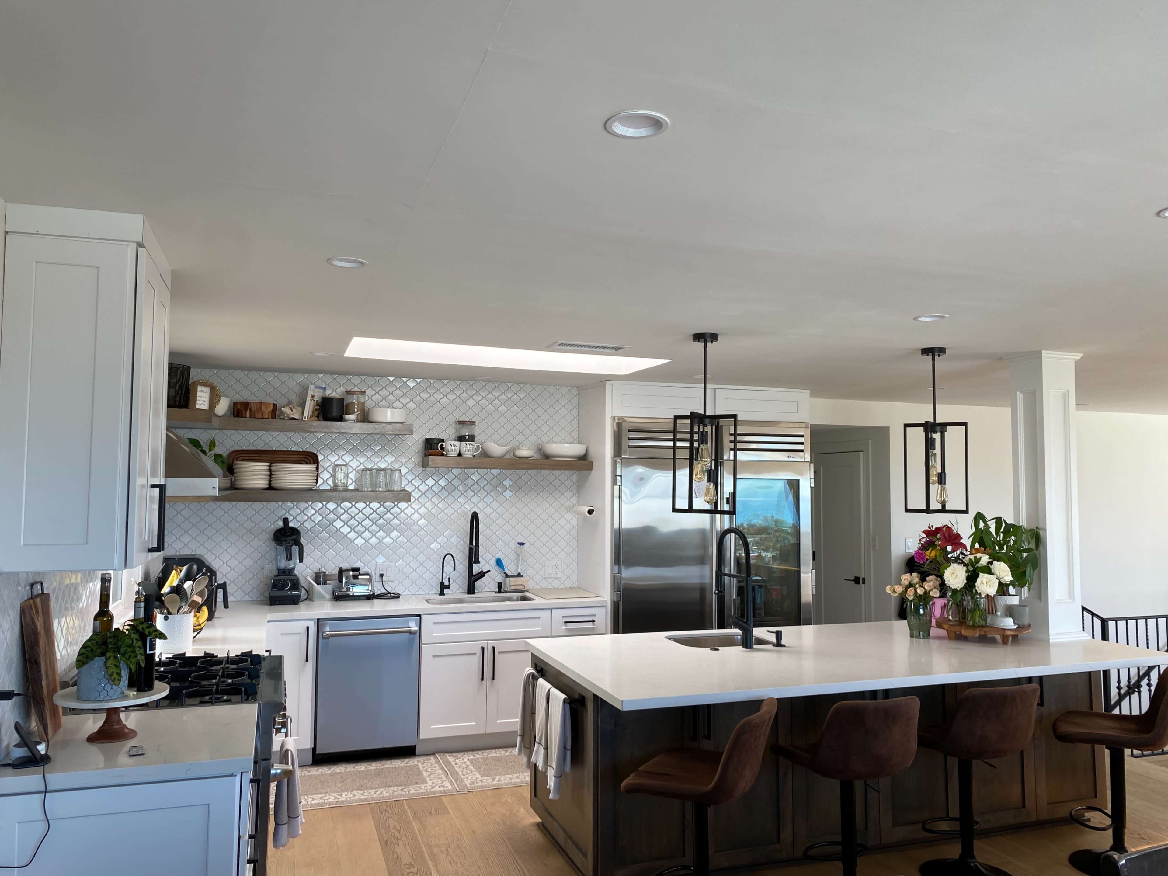 The kitchen features white cabinetry, a large island with brown bar stools, and stainless steel appliances arranged around a tiled backsplash.