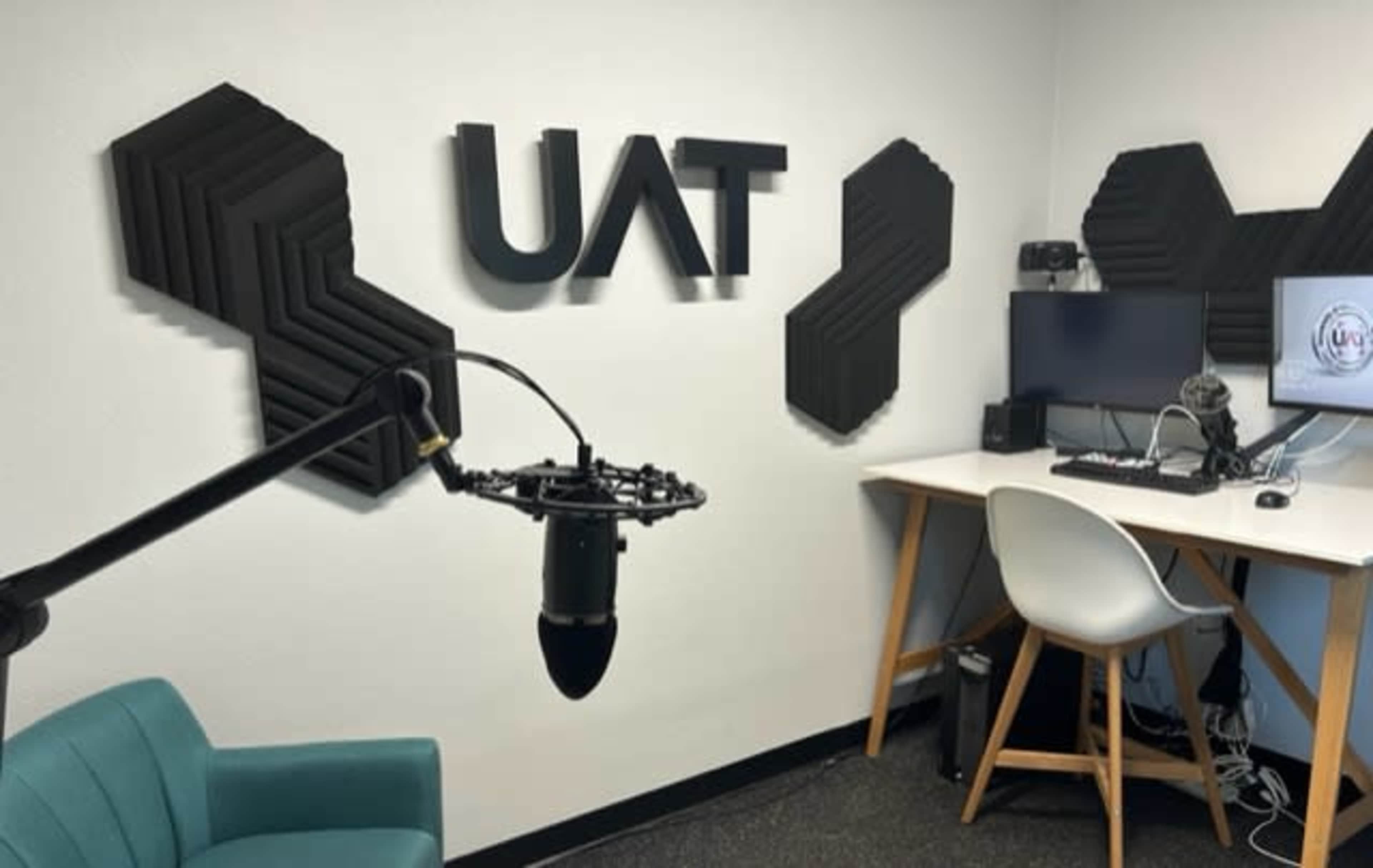 A small recording studio with soundproofing panels on the wall, a microphone on a boom arm, and a desk with a computer and chair.