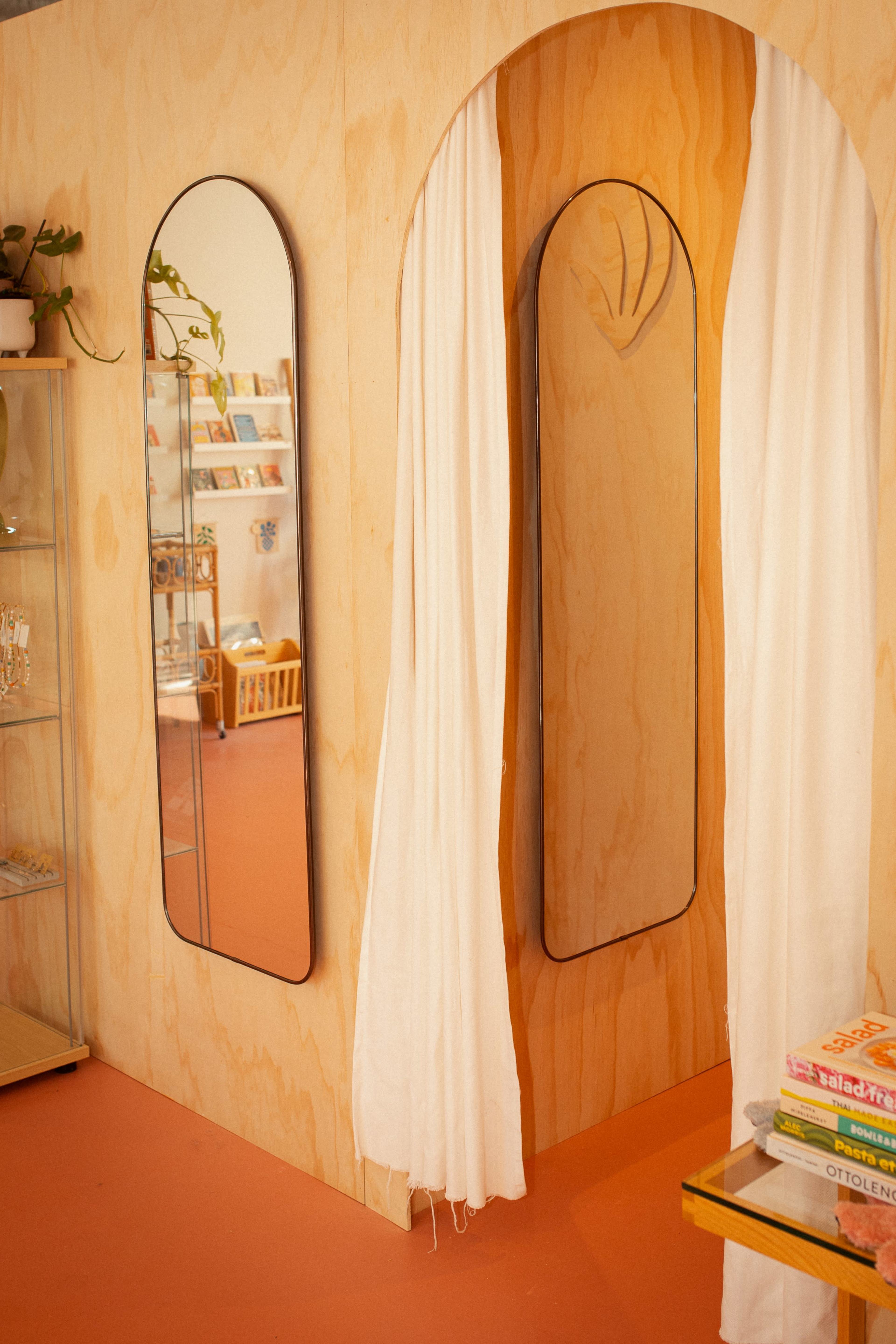 A wooden interior with arched mirrors, a white curtain, and shelves filled with books and decorative items.