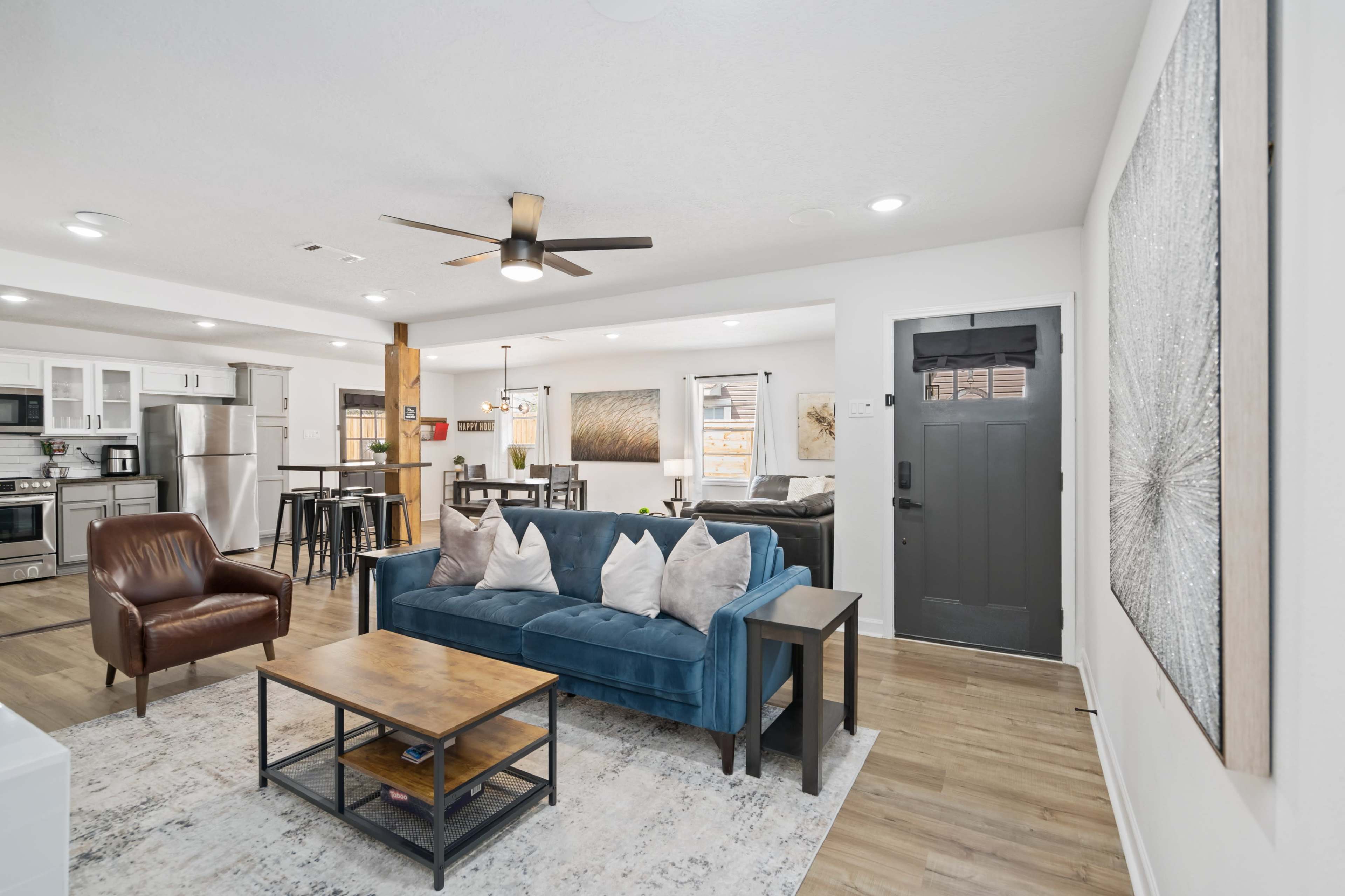 A well-furnished living area featuring a blue sofa, a wooden coffee table, and a dining space with a kitchen visible in the background.