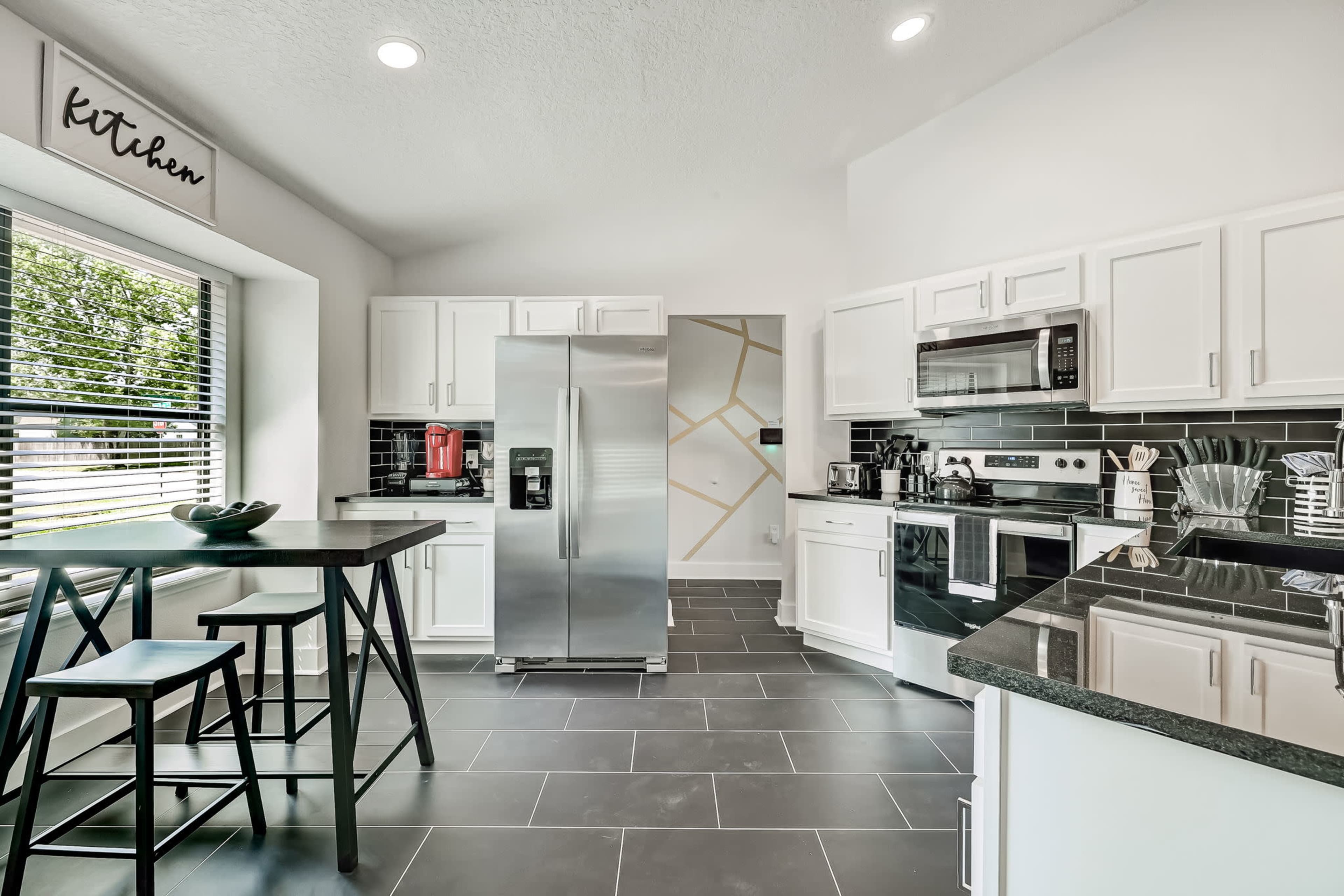 A modern kitchen with white cabinets, a stainless steel refrigerator, and a dark tiled floor.