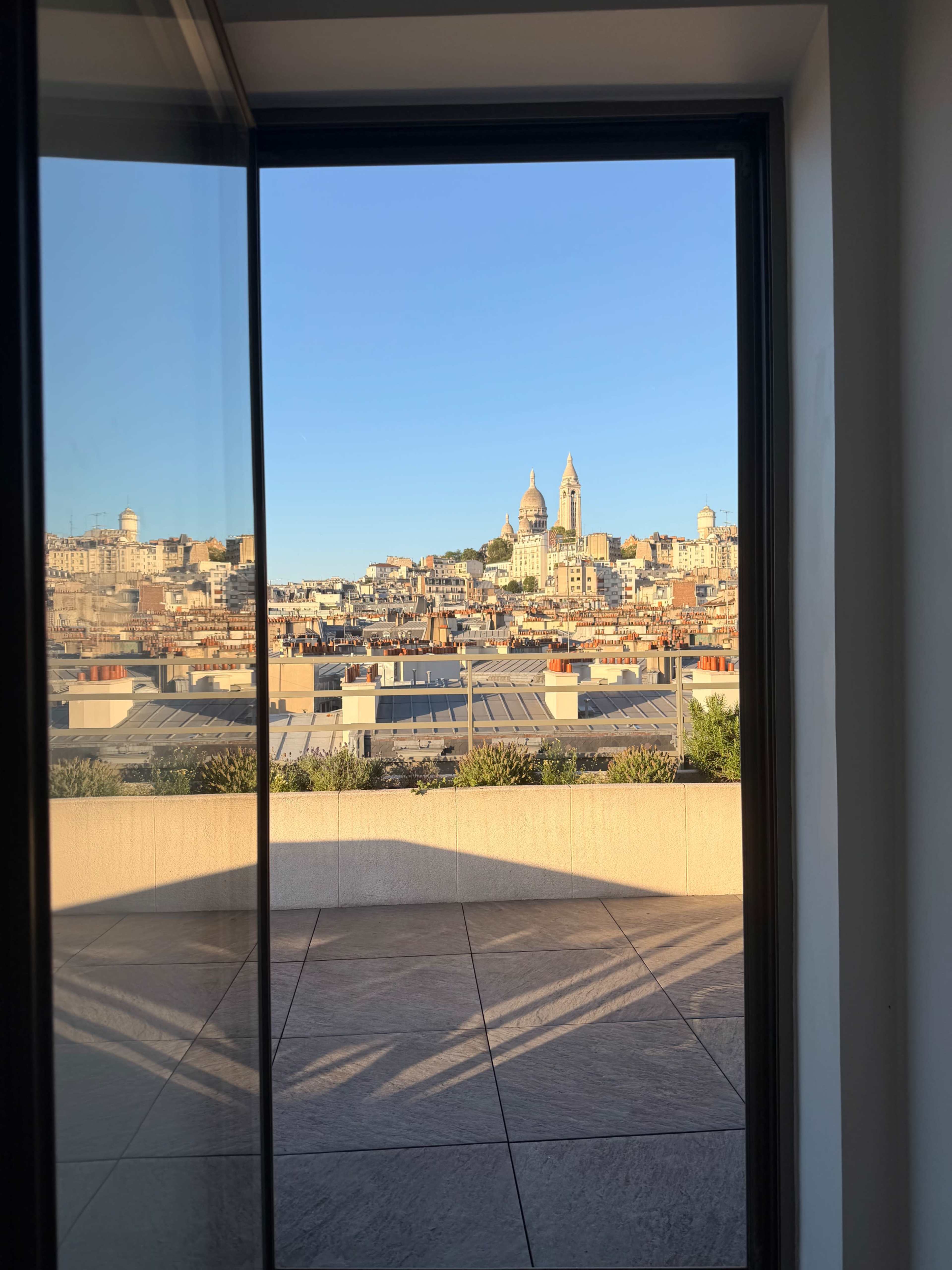 The image shows a view of a cityscape featuring buildings and two towers through an open glass door.