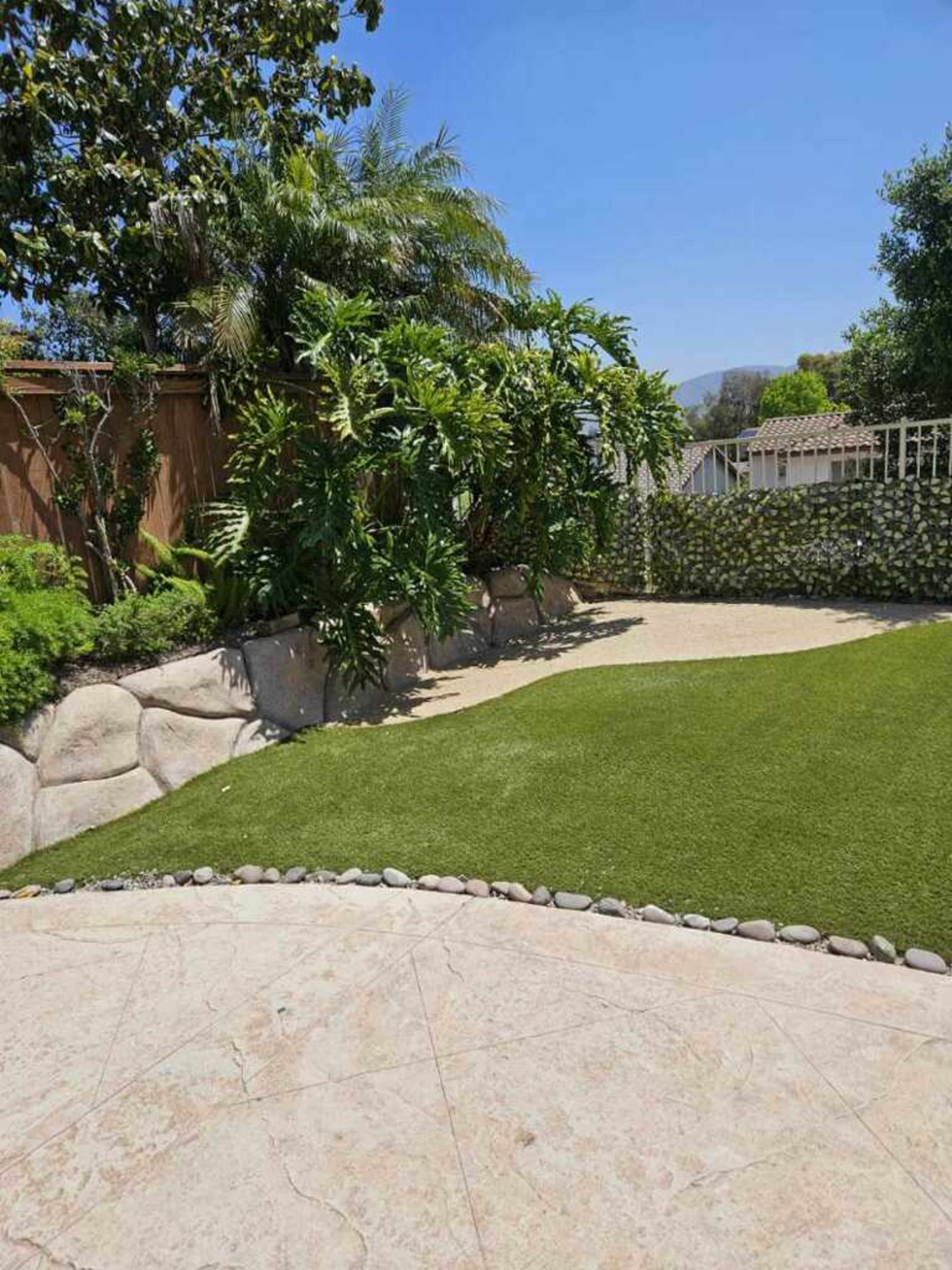A landscaped backyard featuring a grassy area surrounded by tropical plants and a rocky border.