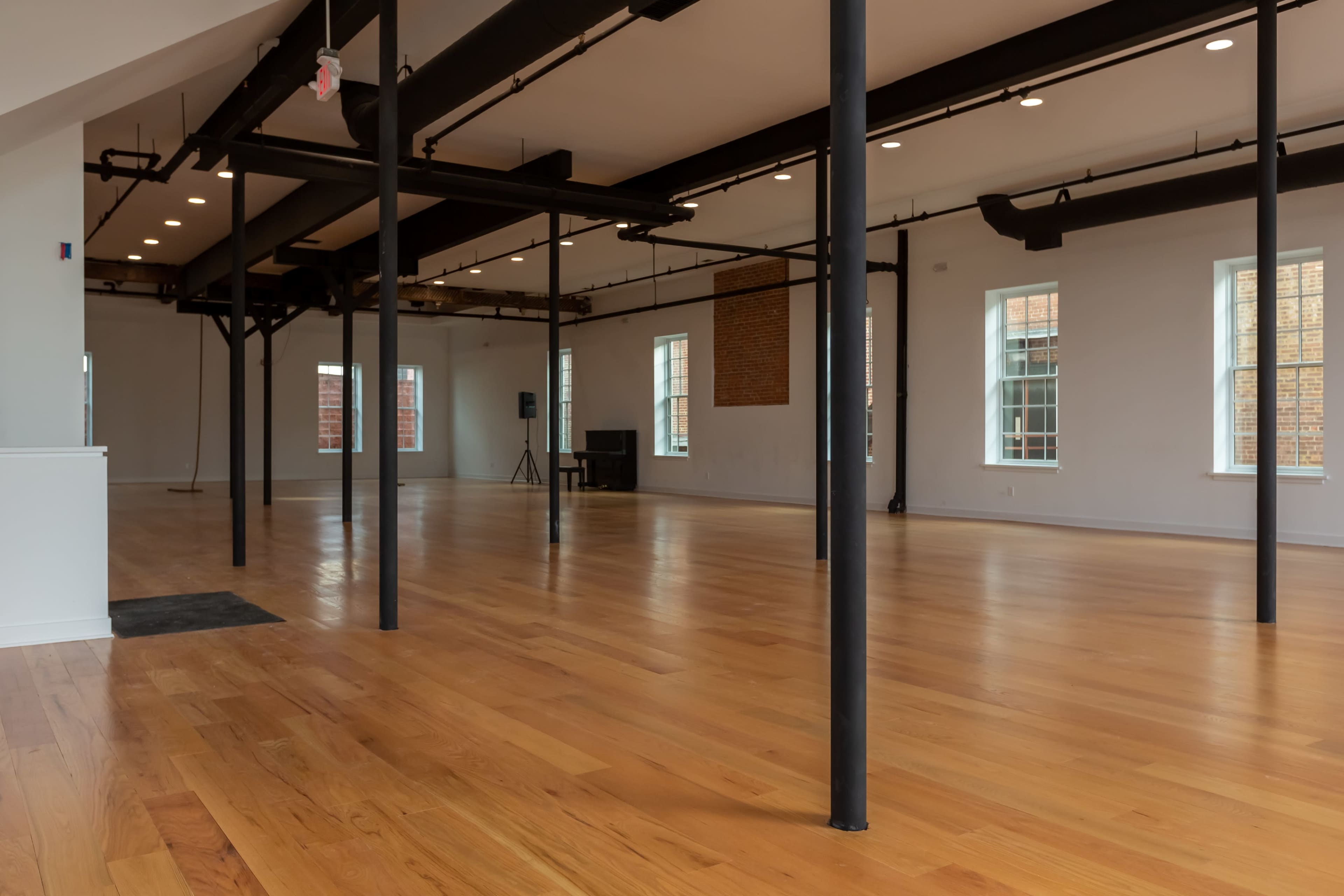 A spacious, empty interior with polished wooden floors, exposed beams, and large windows.