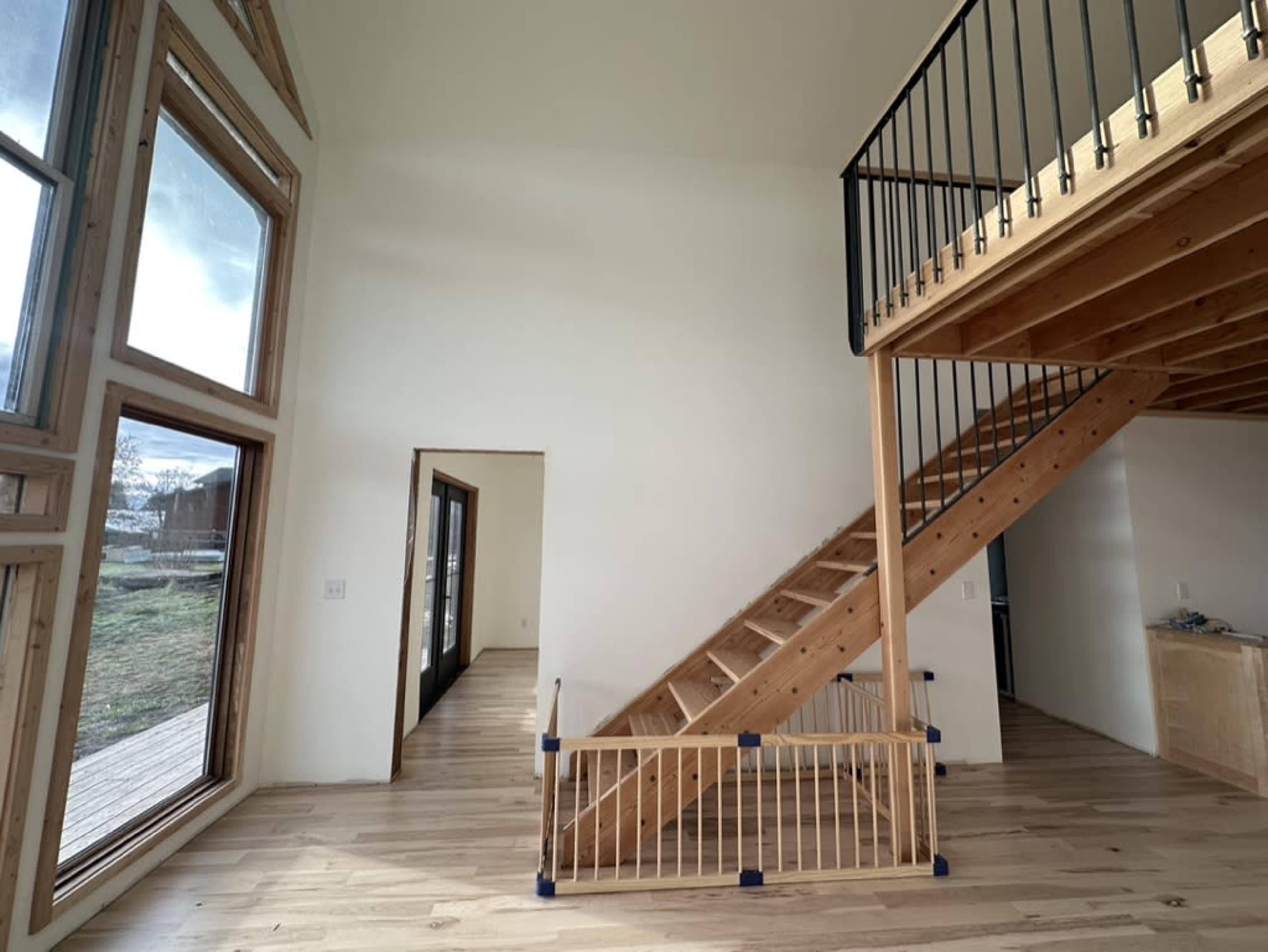 The image shows an interior space with a wooden staircase, large windows, and a light-colored wooden floor.