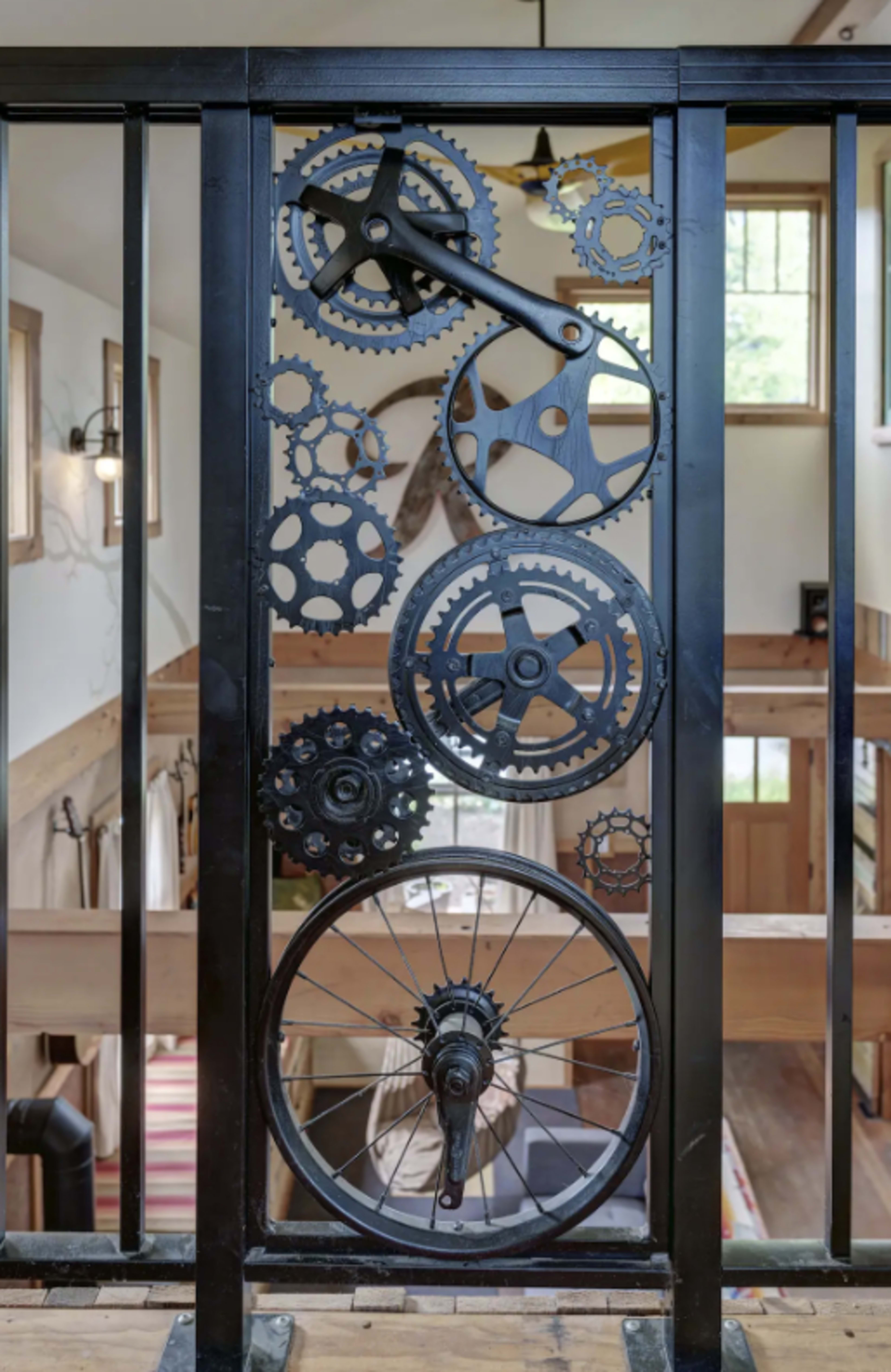 The image shows a decorative metal railing featuring a series of interconnected gears and cogs set against a wooden interior.