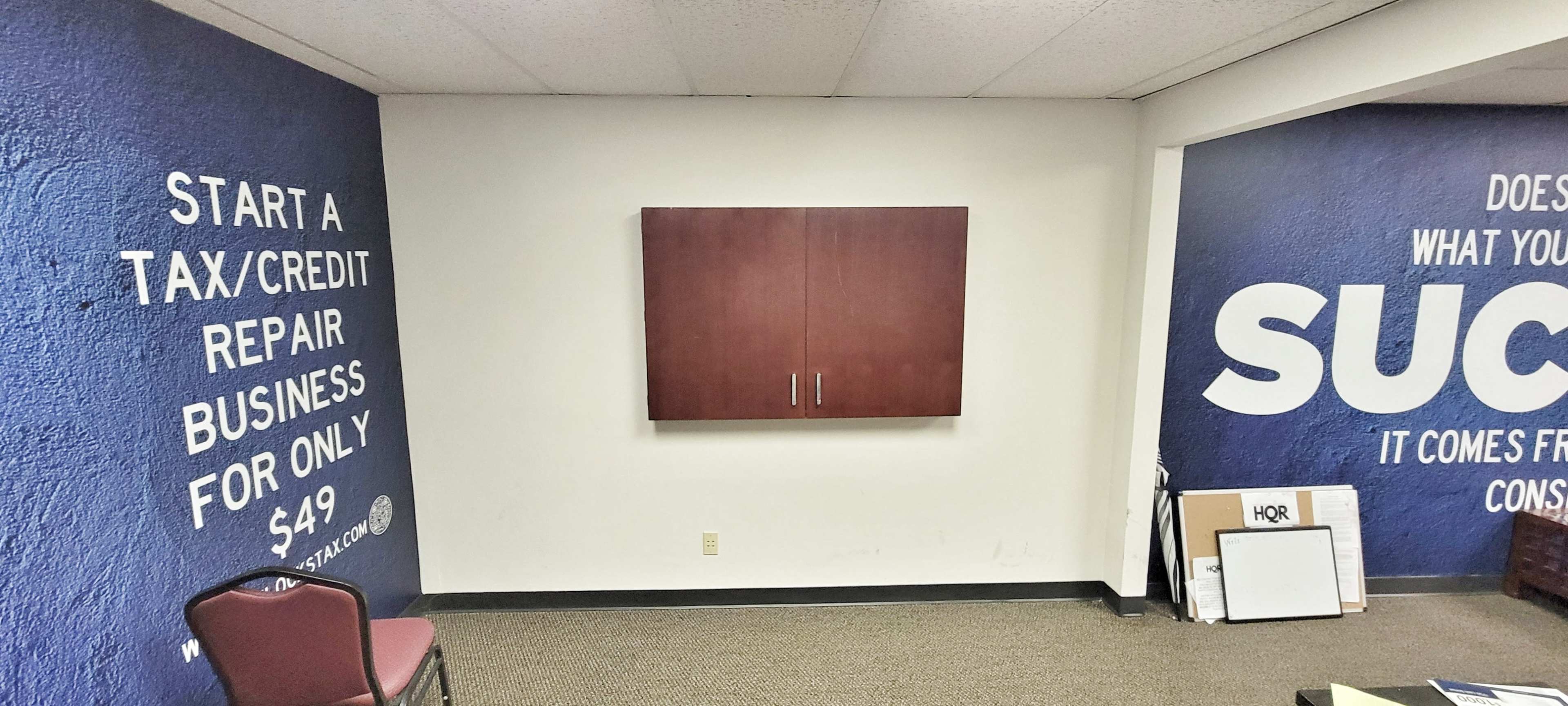 The image shows a room with dark blue walls featuring text about starting a tax/credit repair business, a wooden cabinet on one wall, and a chair in the corner.