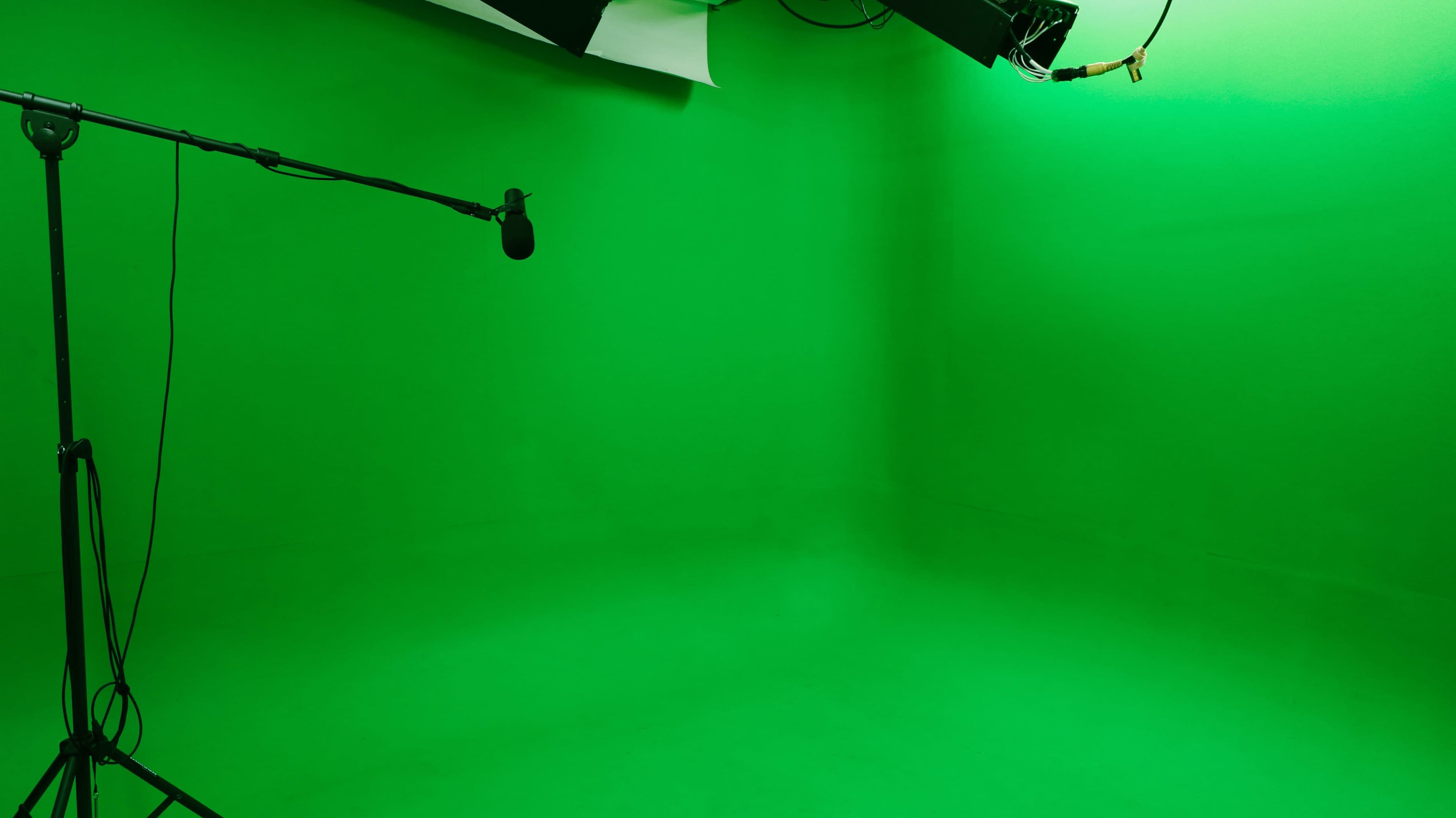 The image shows a bright green studio space with a microphone on a stand and lighting equipment overhead.