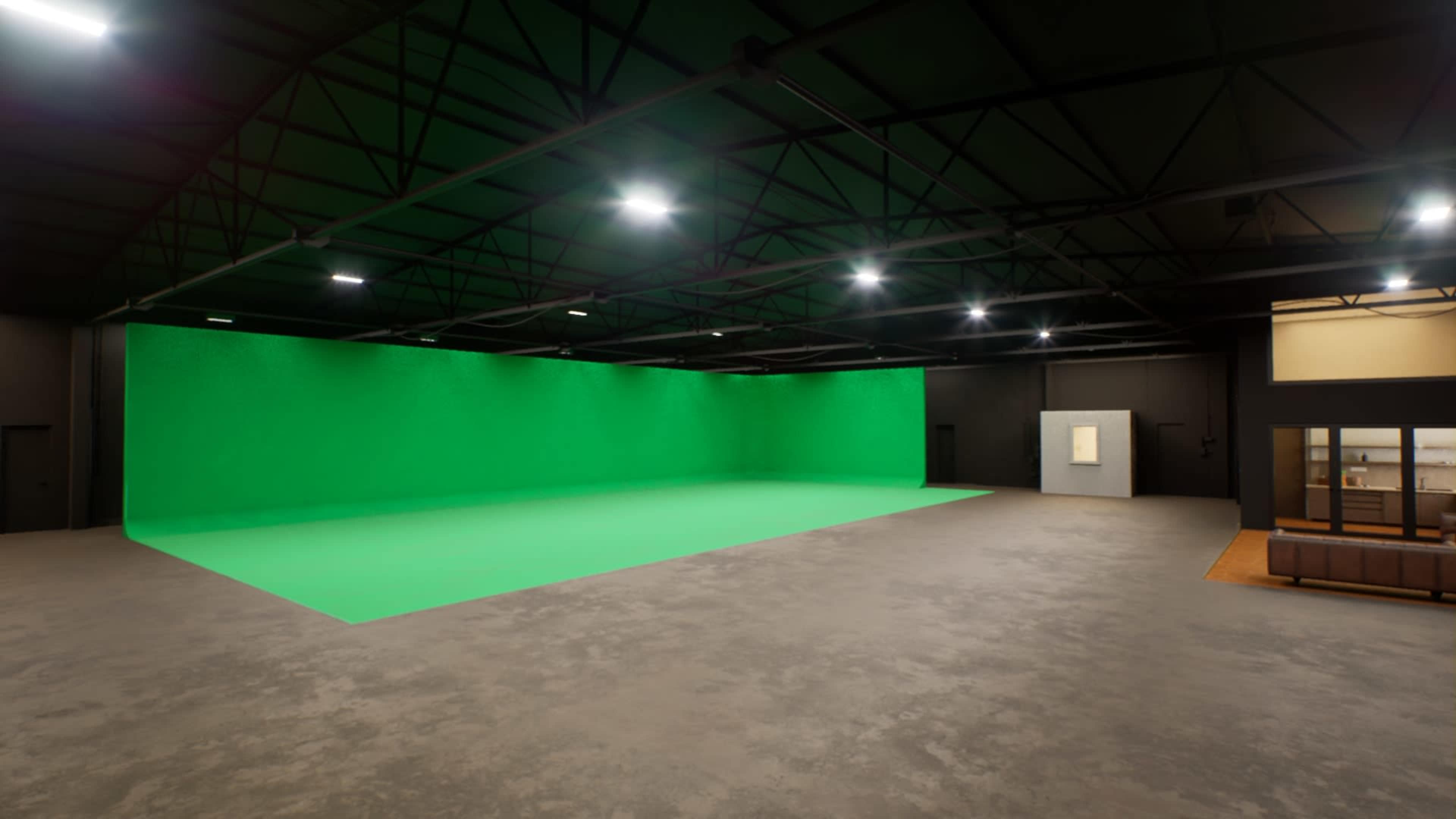 A large industrial space with a green screen backdrop and a light gray concrete floor.