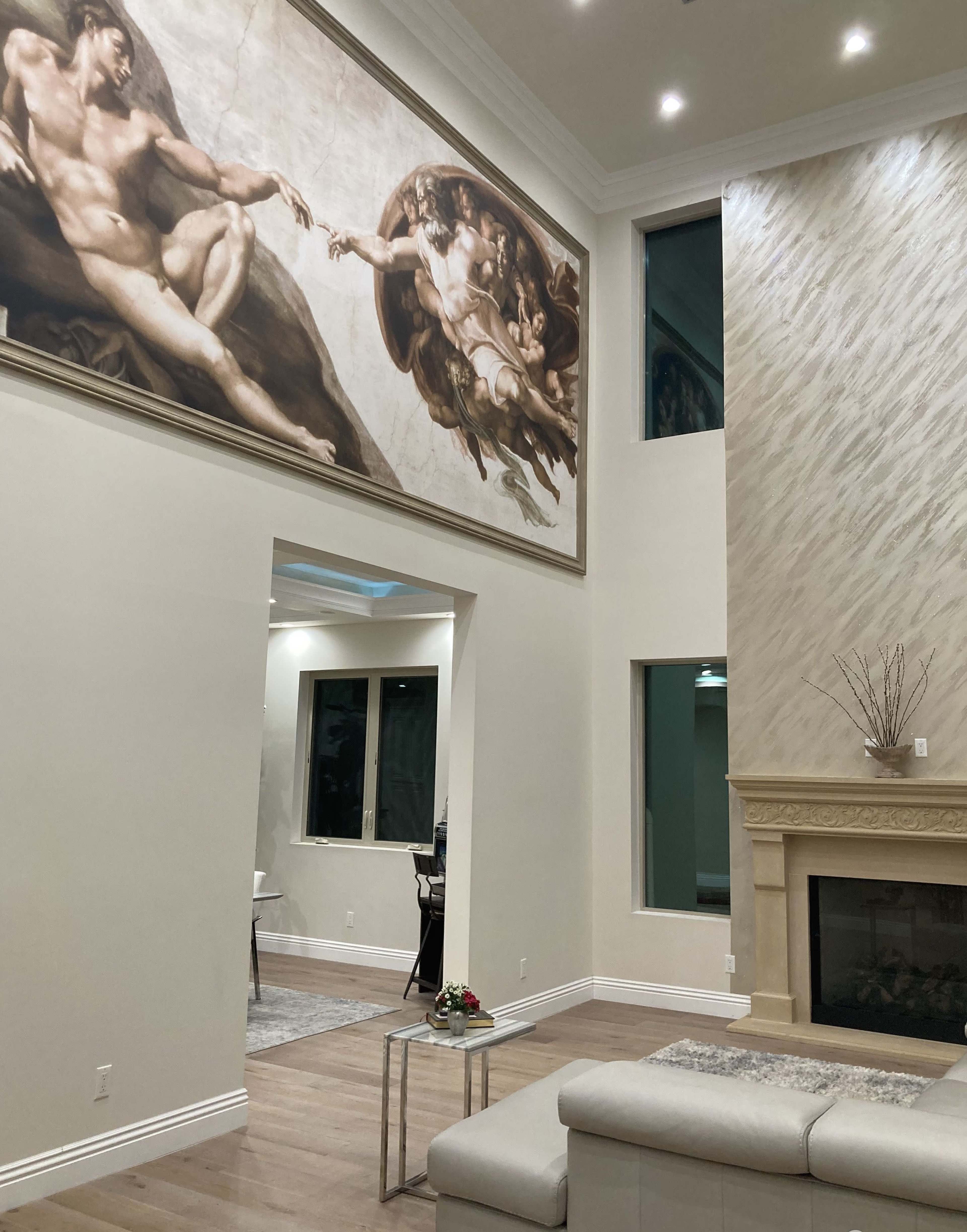 A modern living room with a large mural on the wall, featuring a depiction from Michelangelo's artwork, and a fireplace below it.