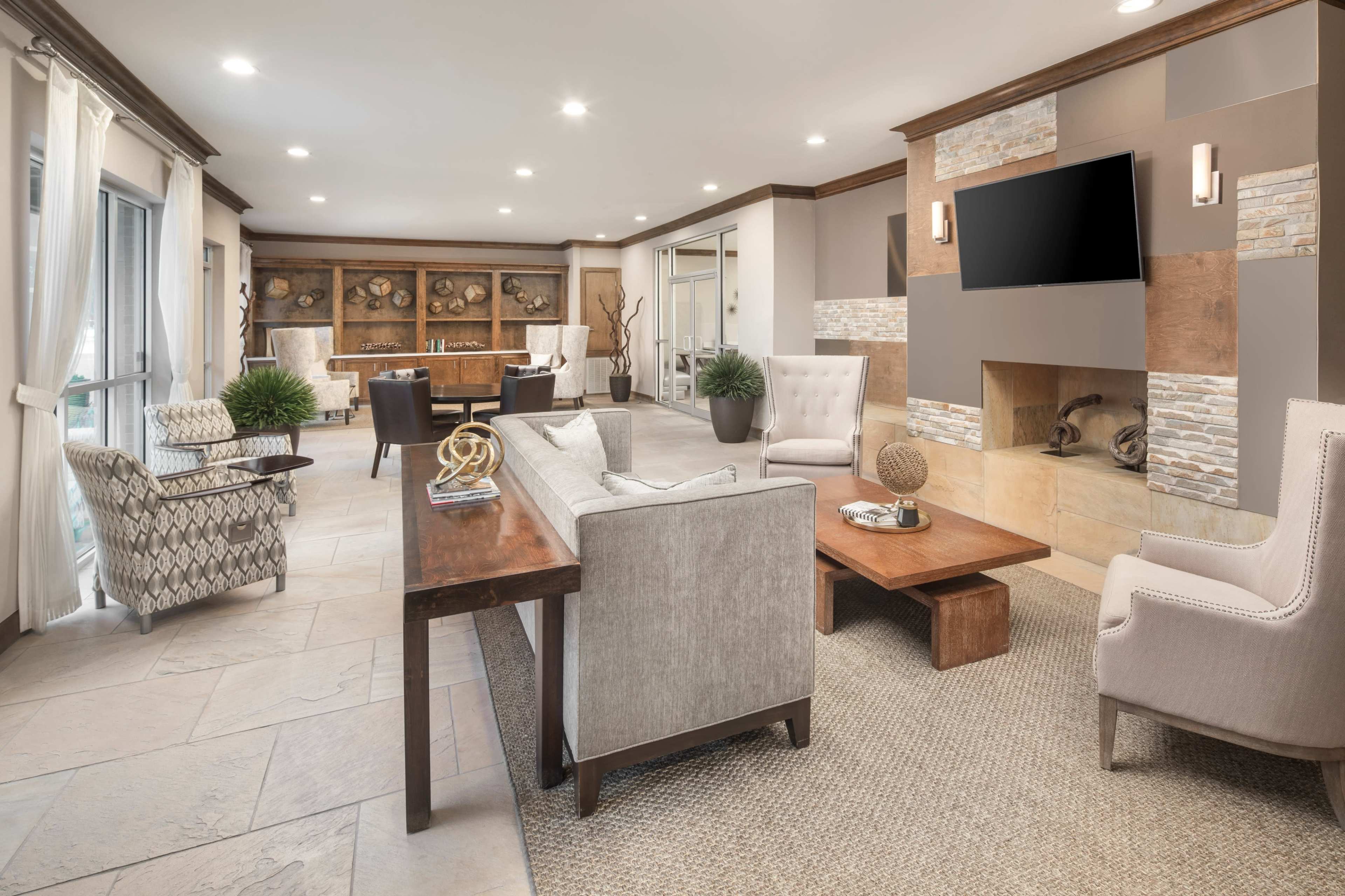 A modern living room with a cozy seating arrangement, a wooden coffee table, and a stone fireplace, complemented by large windows and wooden cabinetry.
