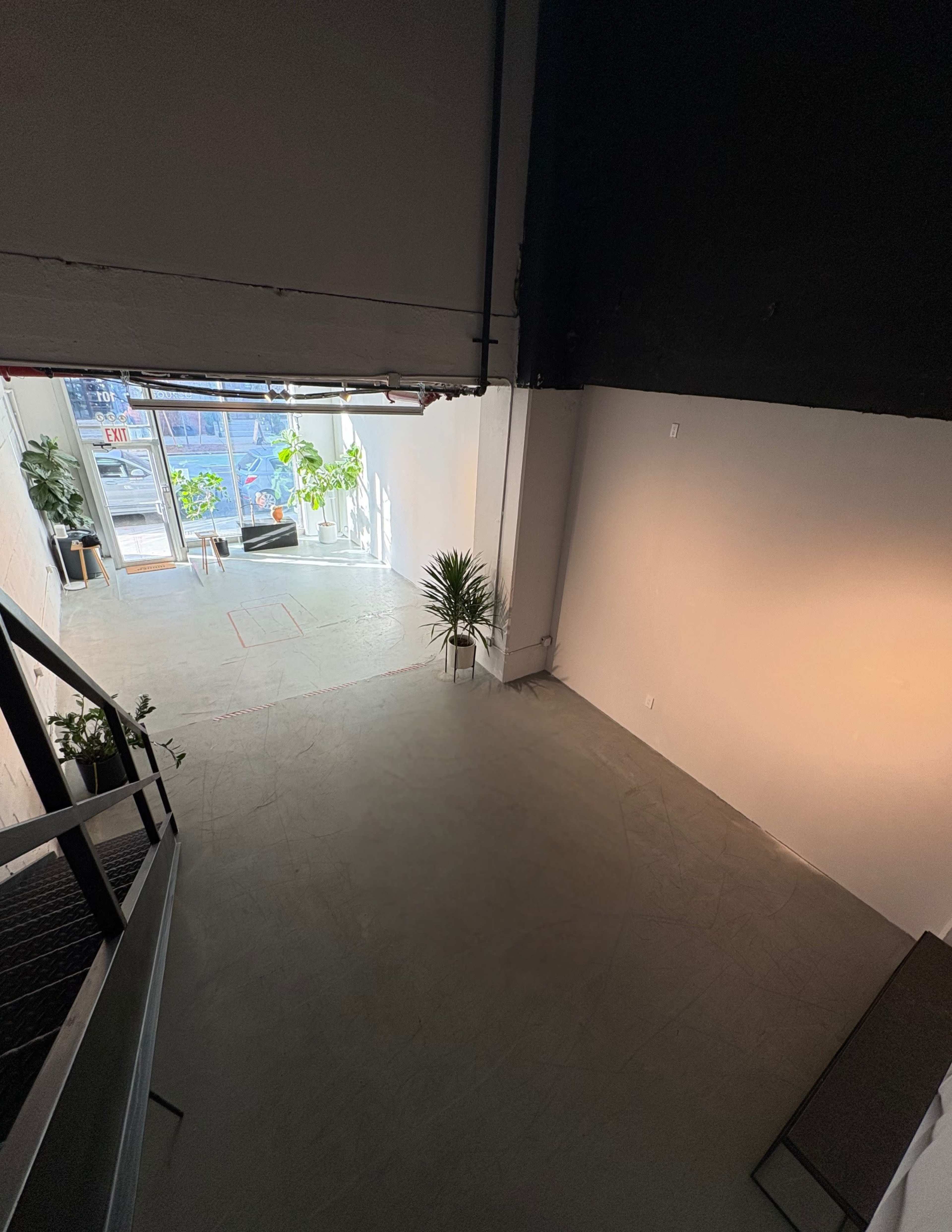 The image shows a spacious interior with a staircase leading down to an open area that includes plants and large windows.