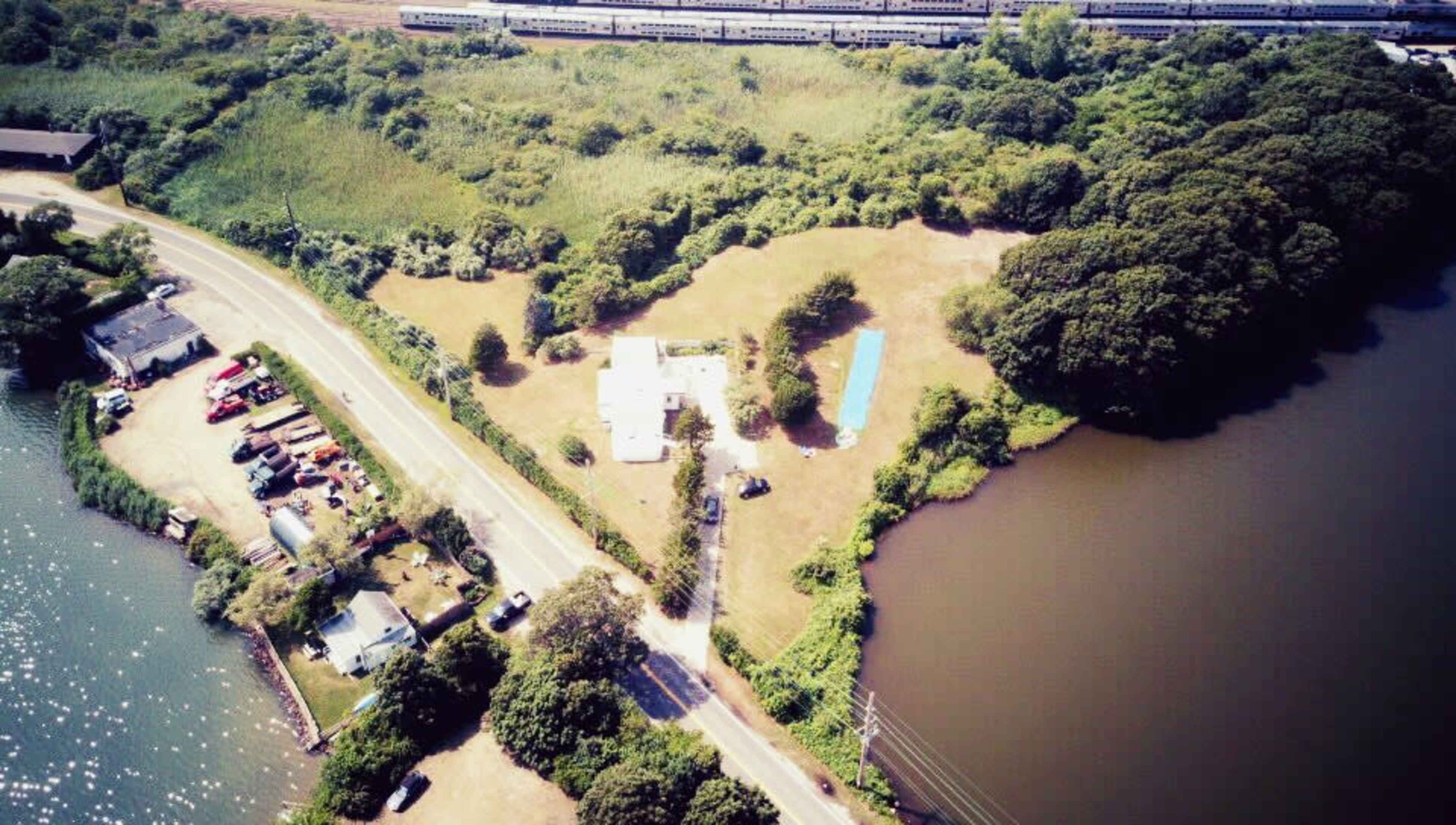 An aerial view of a property near a river, with a house, a pool, and dense greenery surrounding the area.