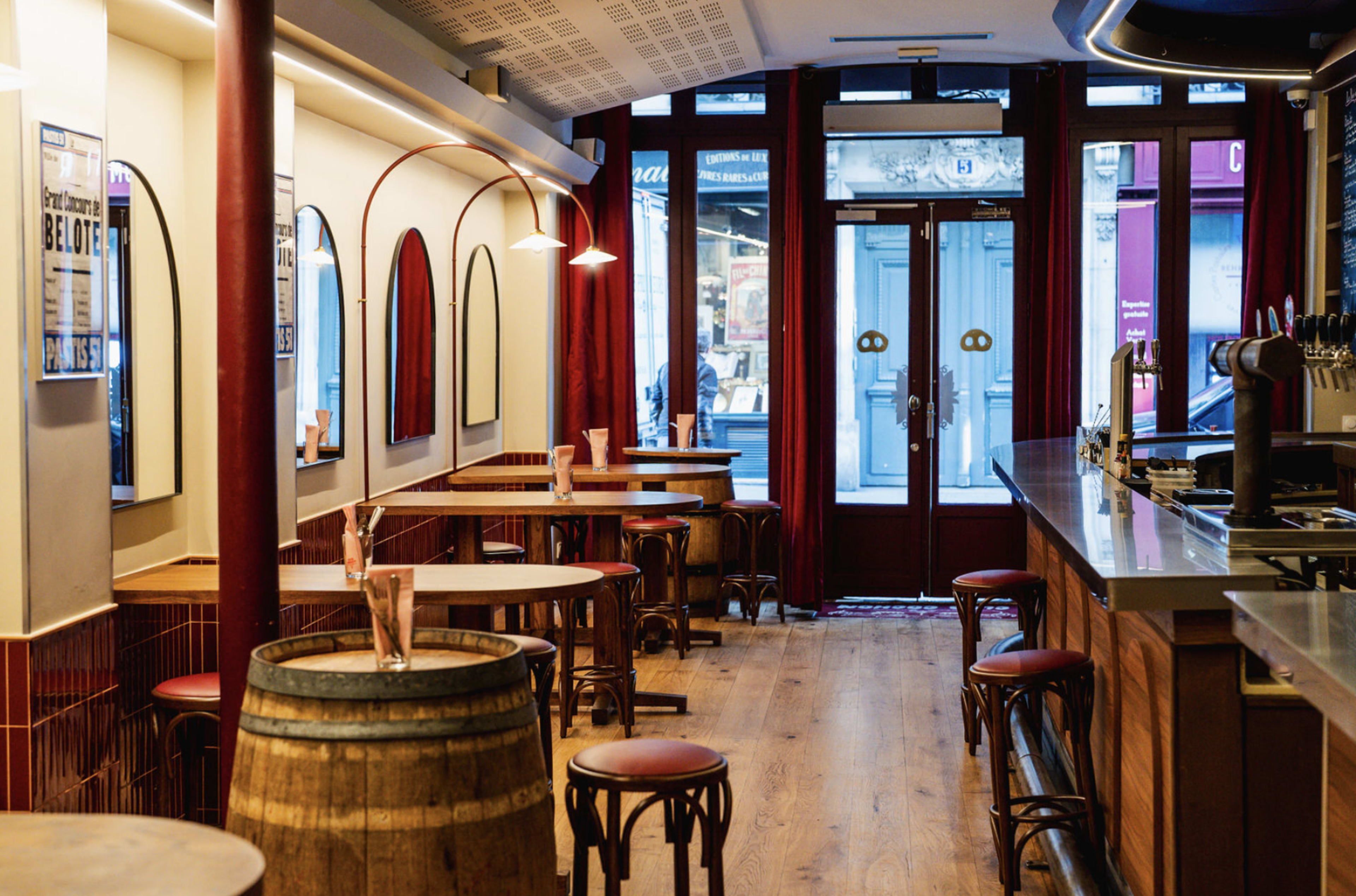 The image shows an empty restaurant interior with wooden floors, round tables, and chairs, featuring a bar area along one side.