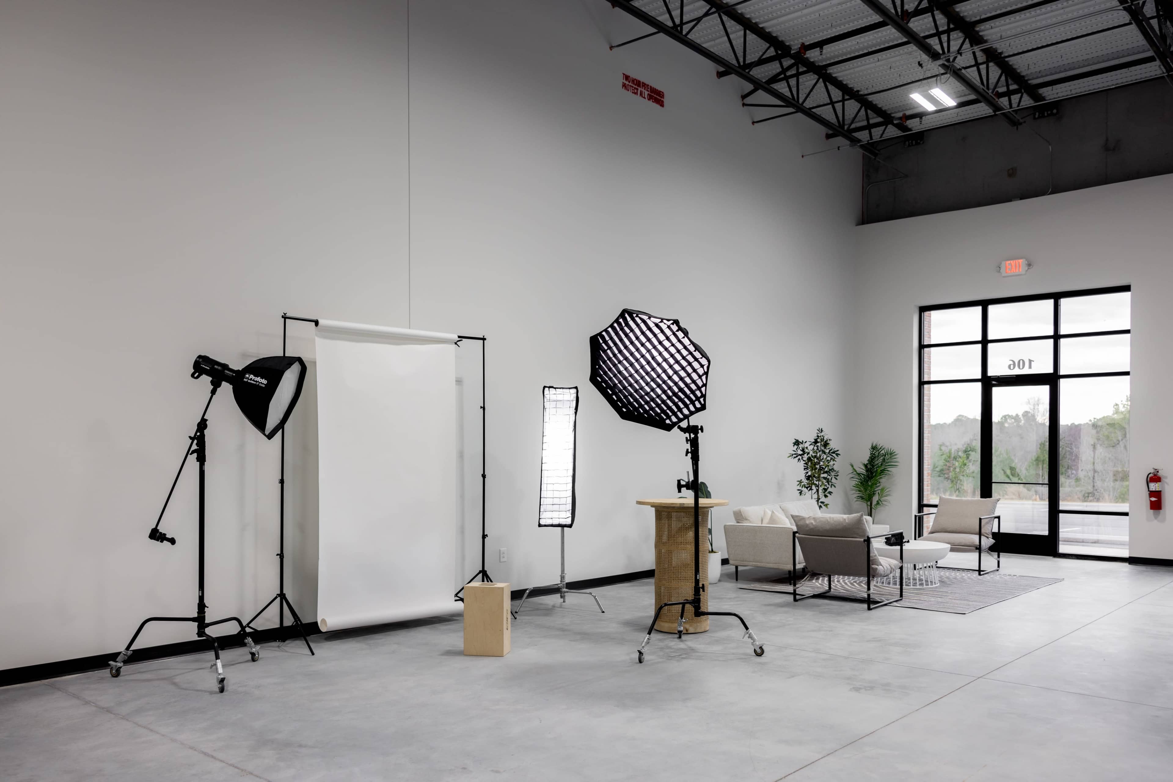 A spacious photography studio featuring a white backdrop, various lighting equipment, and a seating area.