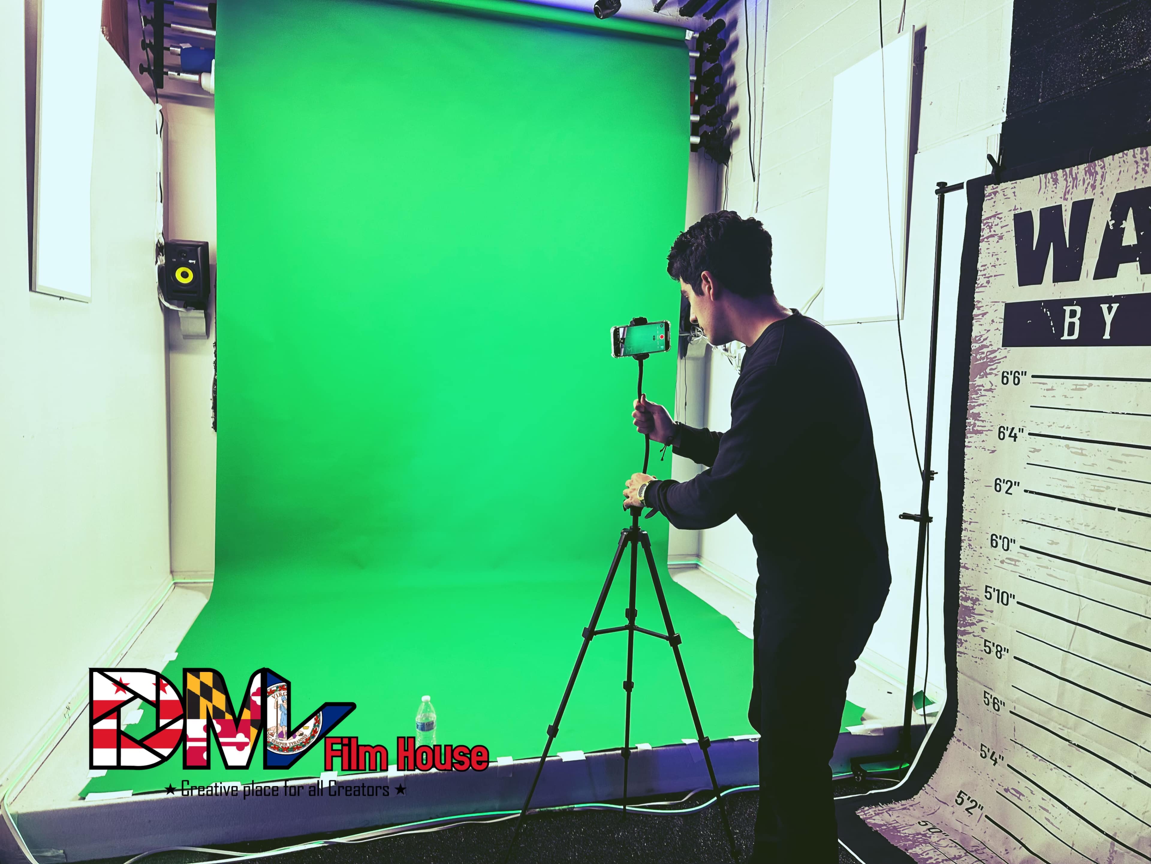 A person sets up a smartphone on a tripod in front of a green screen in a film studio.