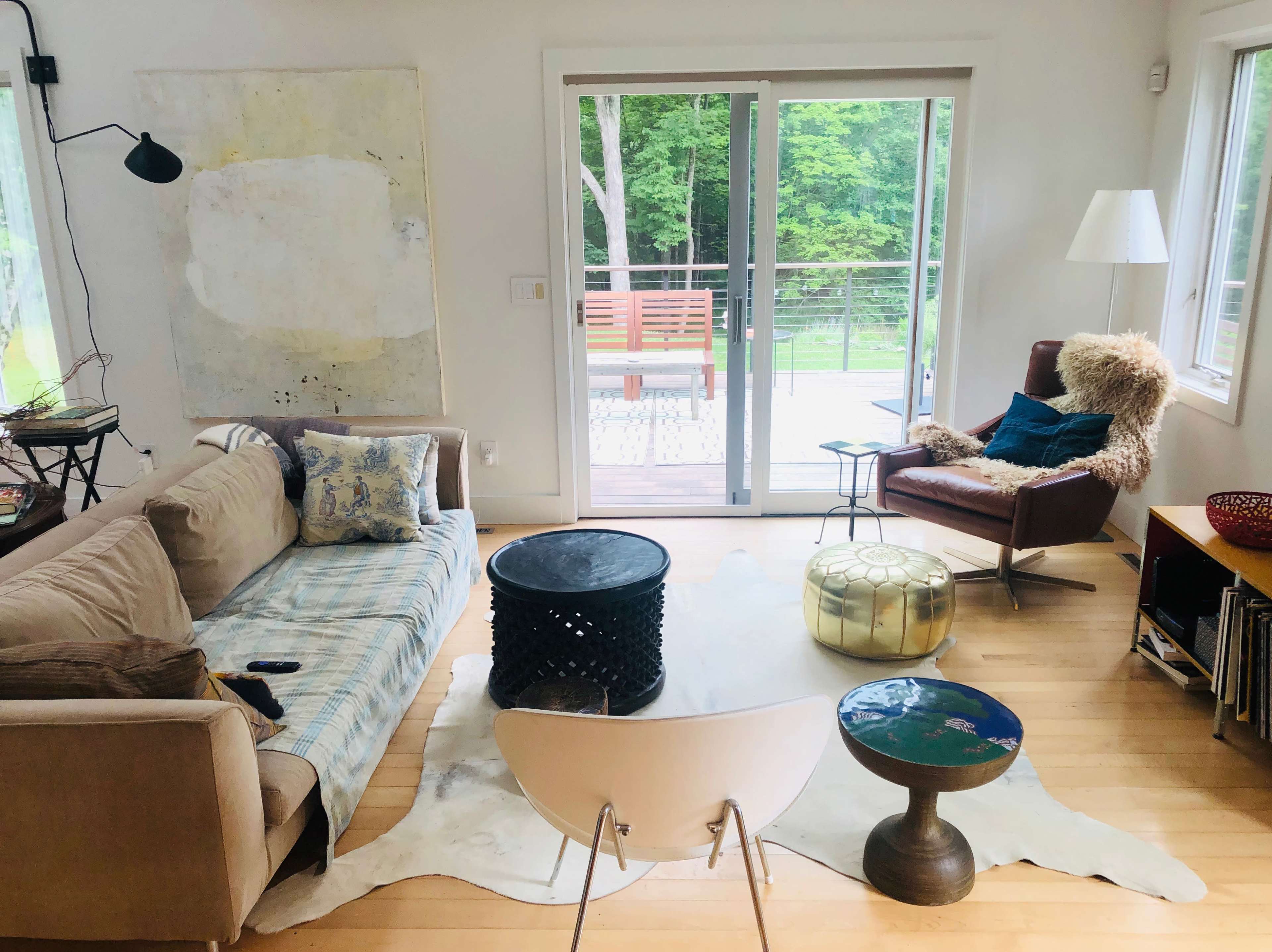 The image shows a modern living room with a couch, a coffee table, and a chair, overlooking a patio and a green outdoor space.