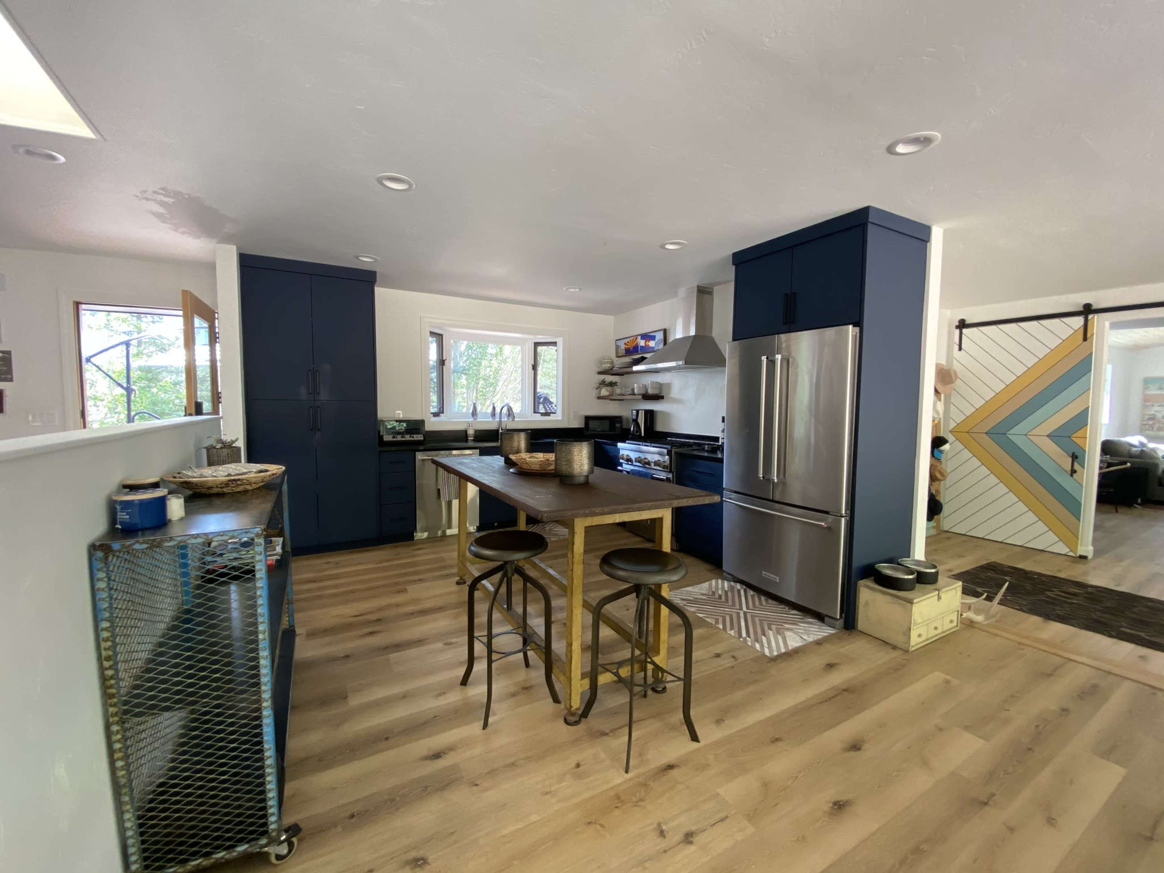 A modern kitchen with dark blue cabinets, stainless steel appliances, and a wooden dining table with metal chairs.