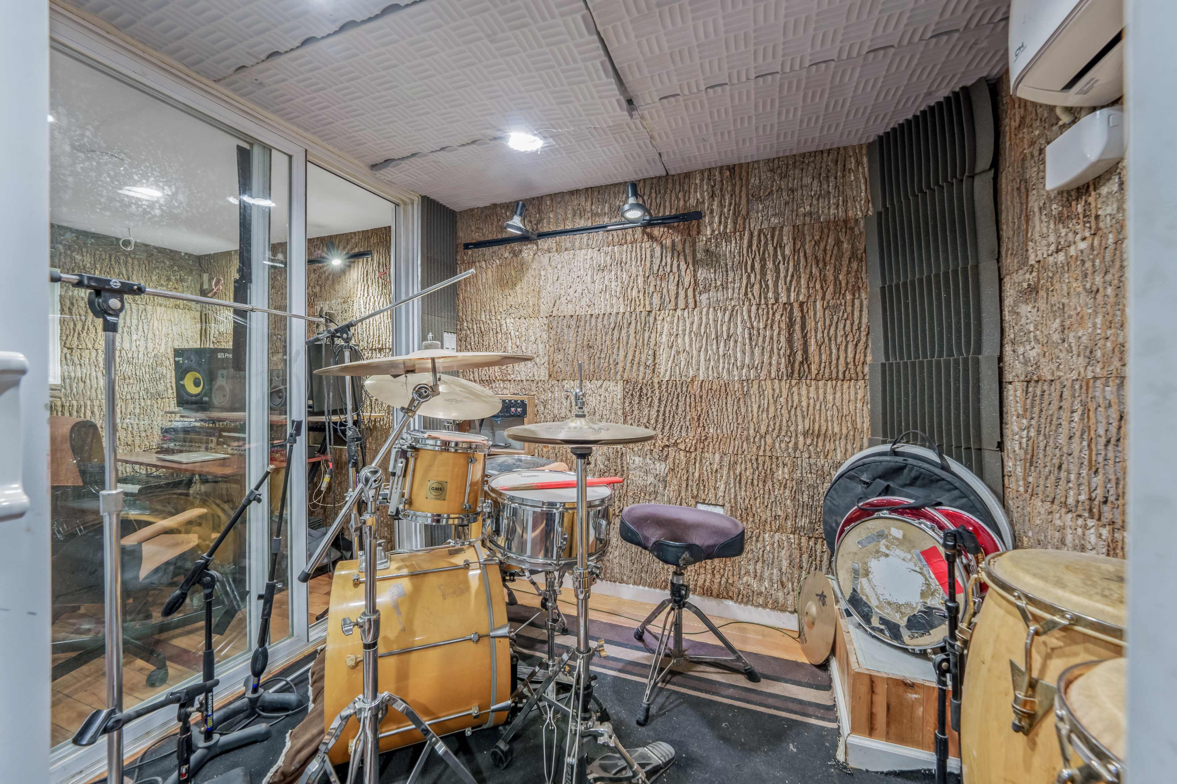 The image shows a soundproof recording studio featuring a drum set and various musical instruments arranged on the floor.