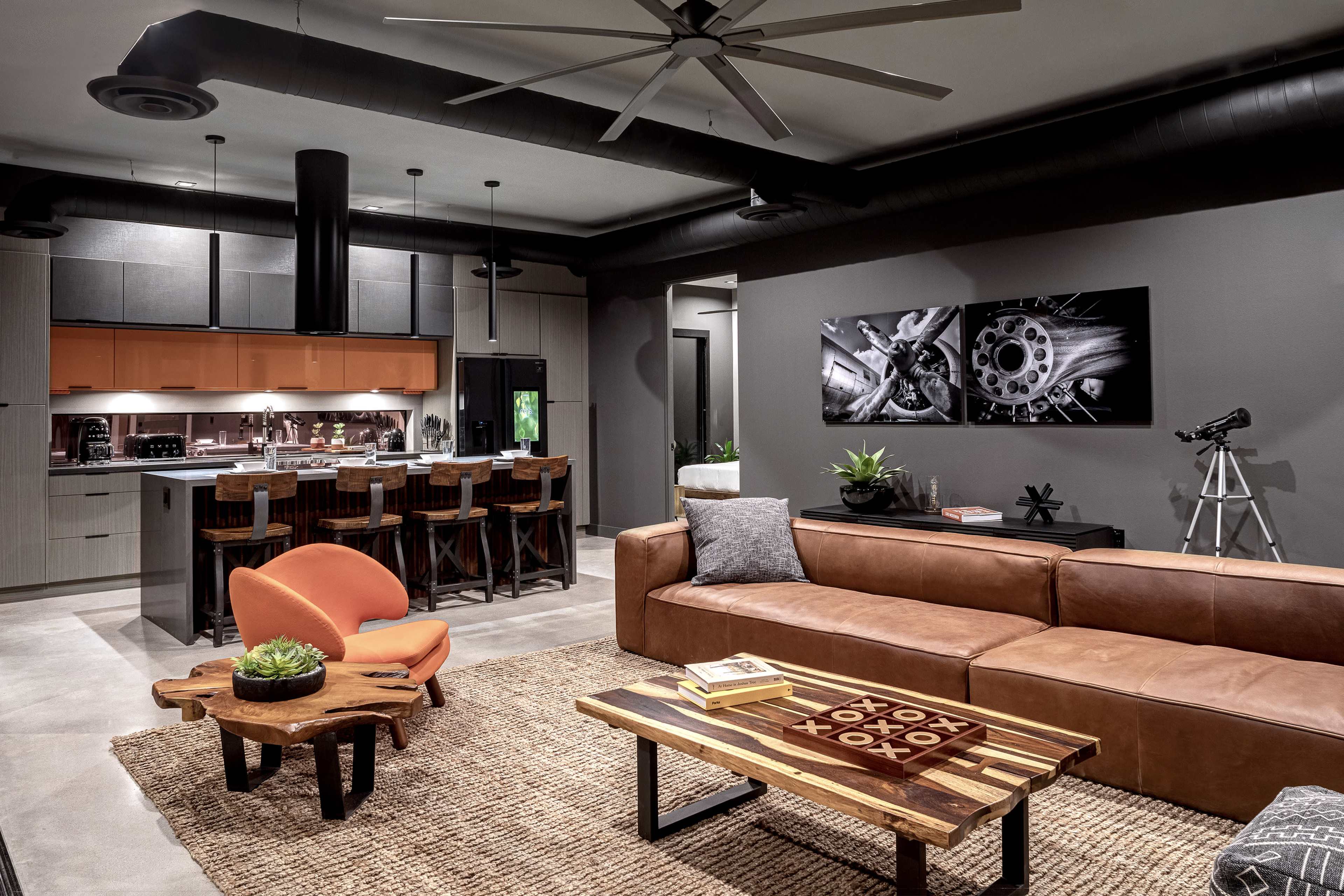 The image shows a modern living room with a brown leather sofa, a wooden coffee table, and a stylish kitchen area with bar seating in the background.