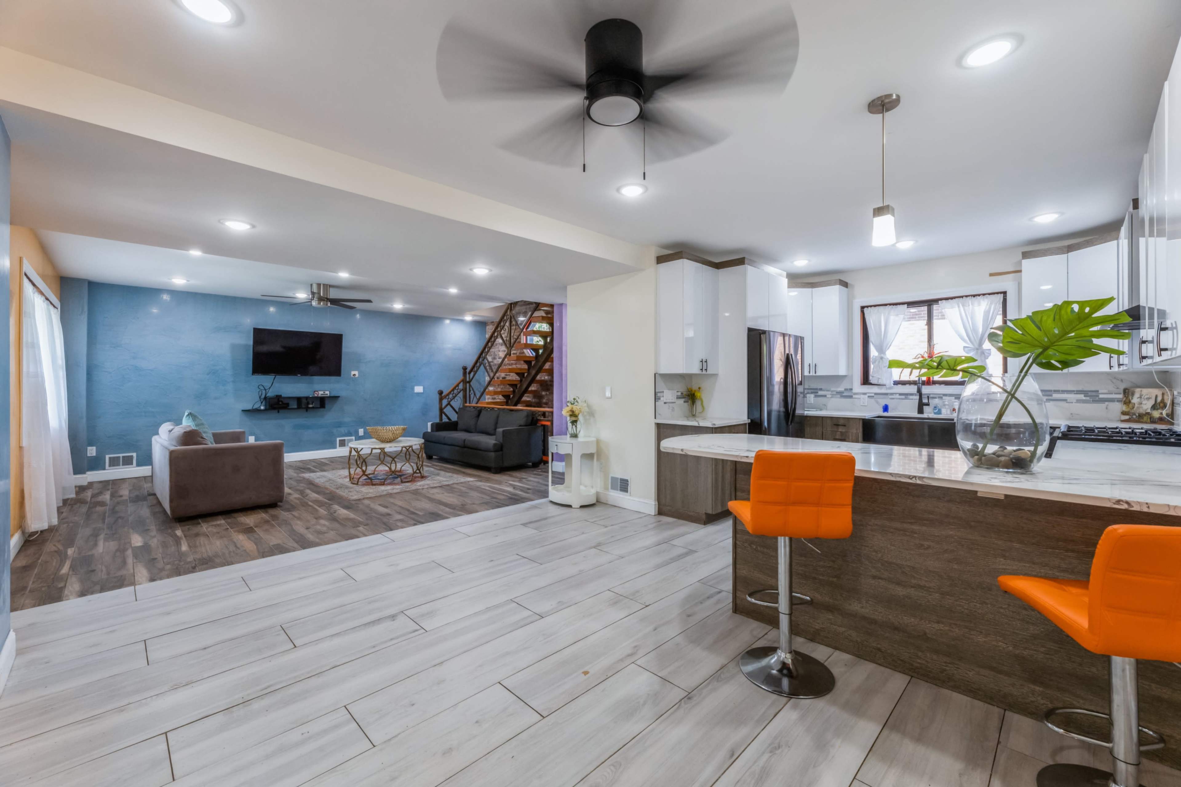 A modern open-concept living area featuring a kitchen with a breakfast bar, a dining space, and a cozy seating area with a staircase visible in the background.