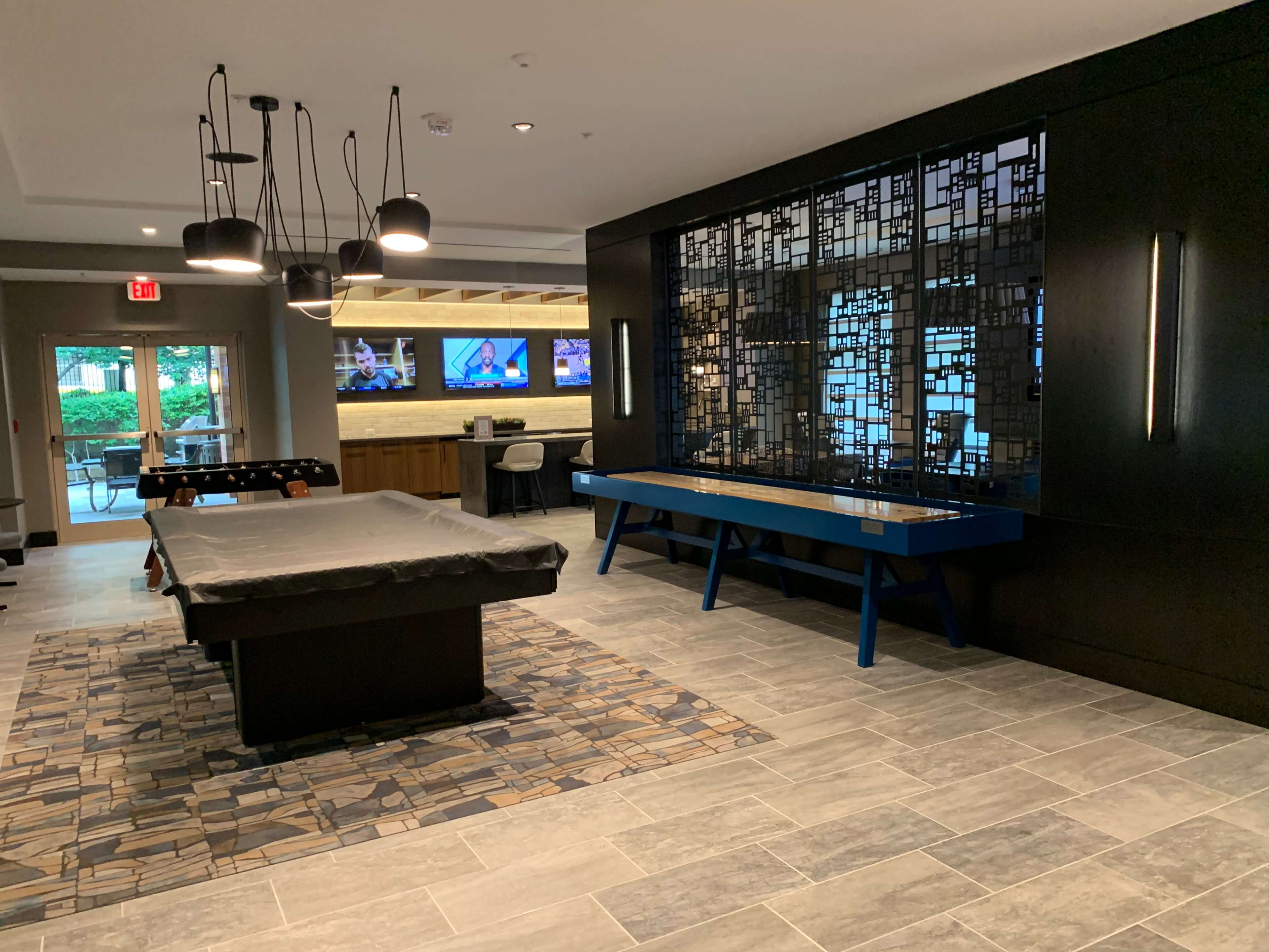 A modern recreation room featuring a pool table, a decorative wall panel, and screens mounted on the wall displaying sports.