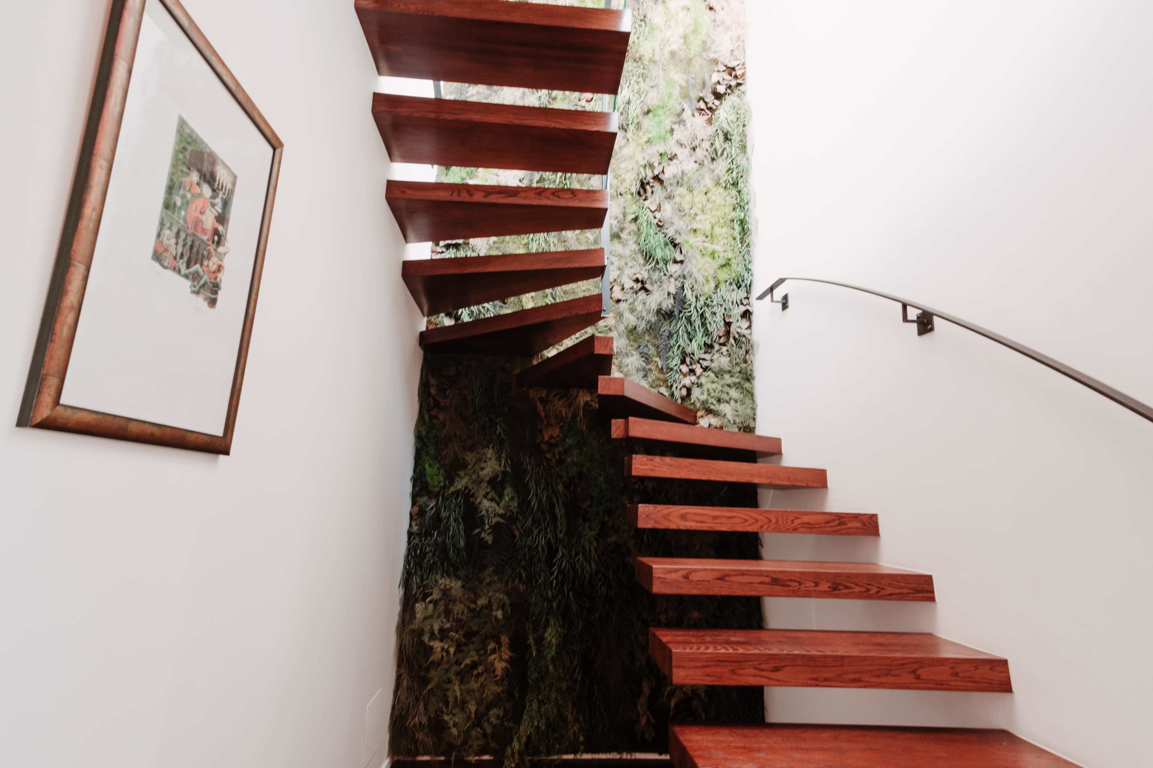 A curved wooden staircase ascends alongside a wall covered in greenery.
