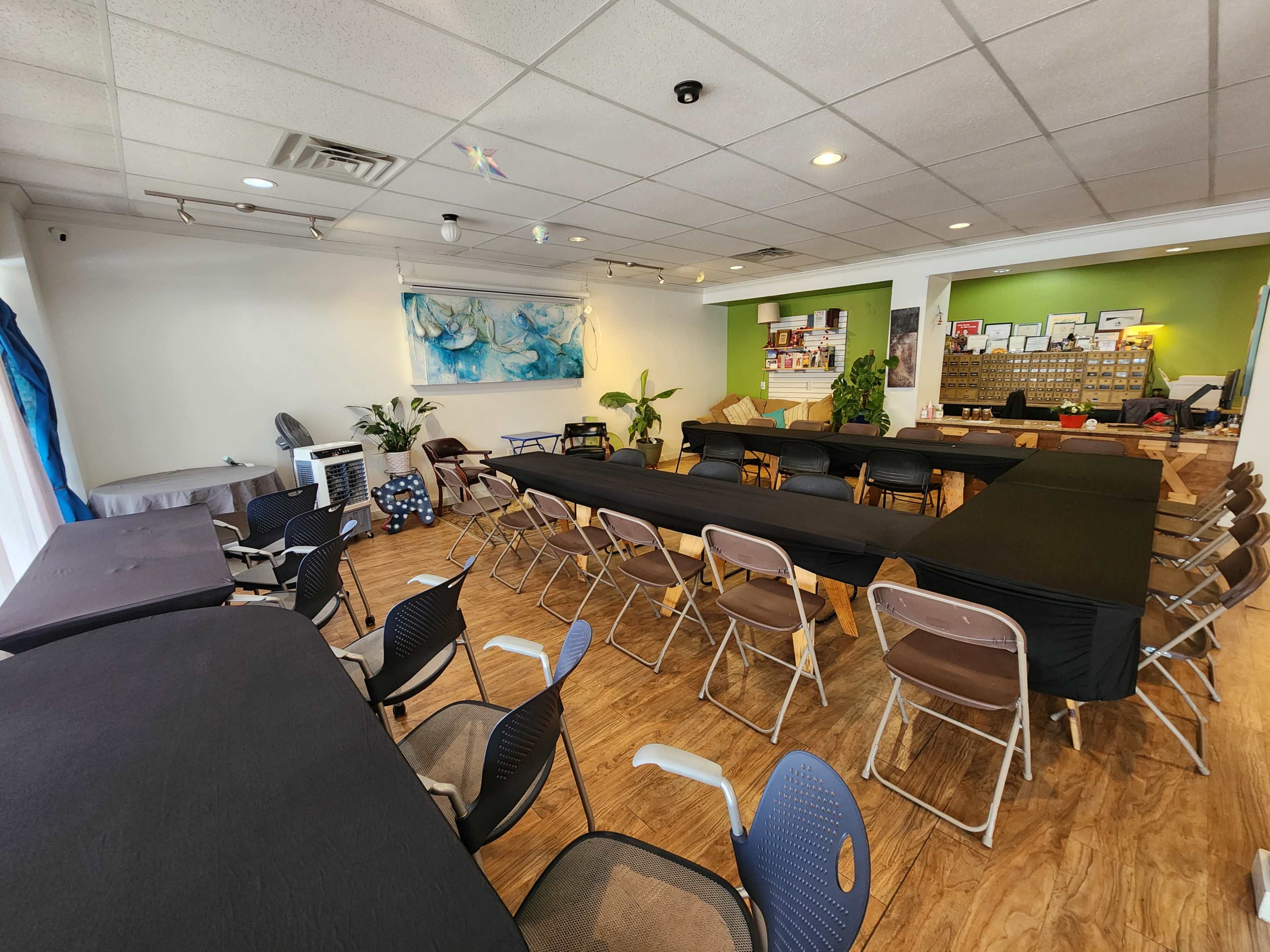 The image shows a spacious room arranged with tables covered in black cloth and chairs positioned around them, ready for an event or meeting.