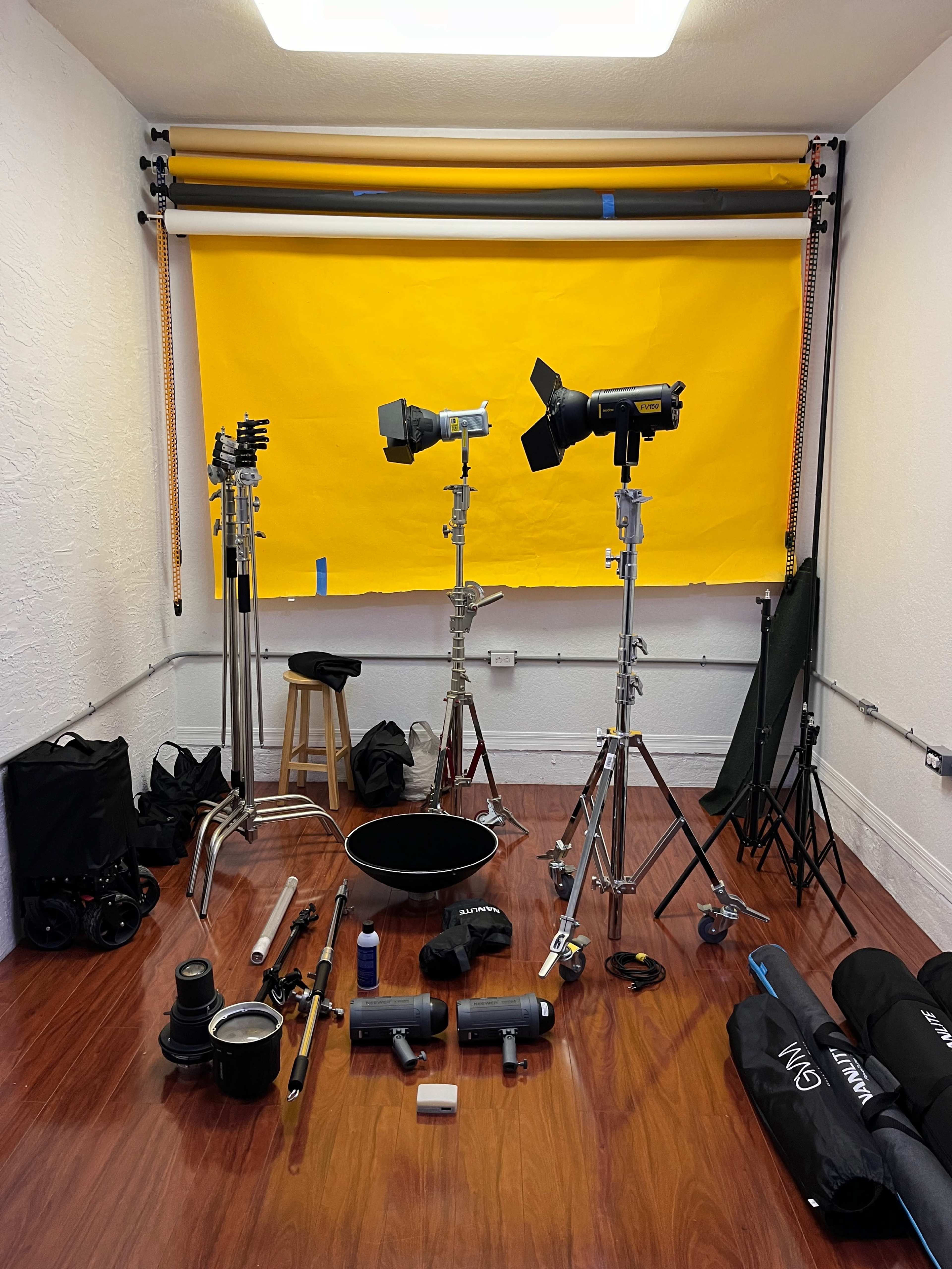 A photography studio set up with various lighting equipment, a yellow backdrop, and scattered accessories on the floor.