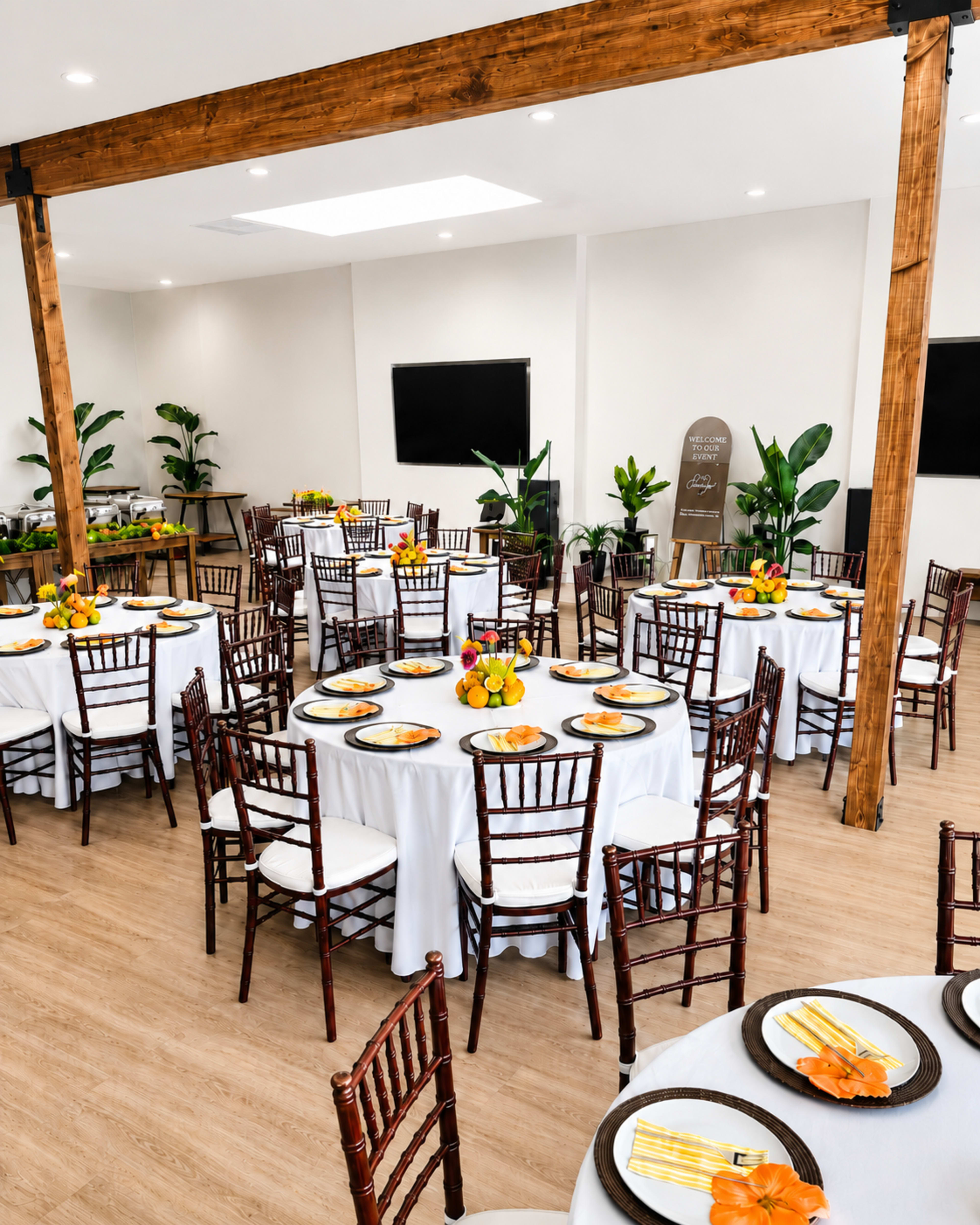 The image shows a banquet hall set up with round tables covered in white tablecloths, each adorned with floral centerpieces and plates, surrounded by wooden chairs.