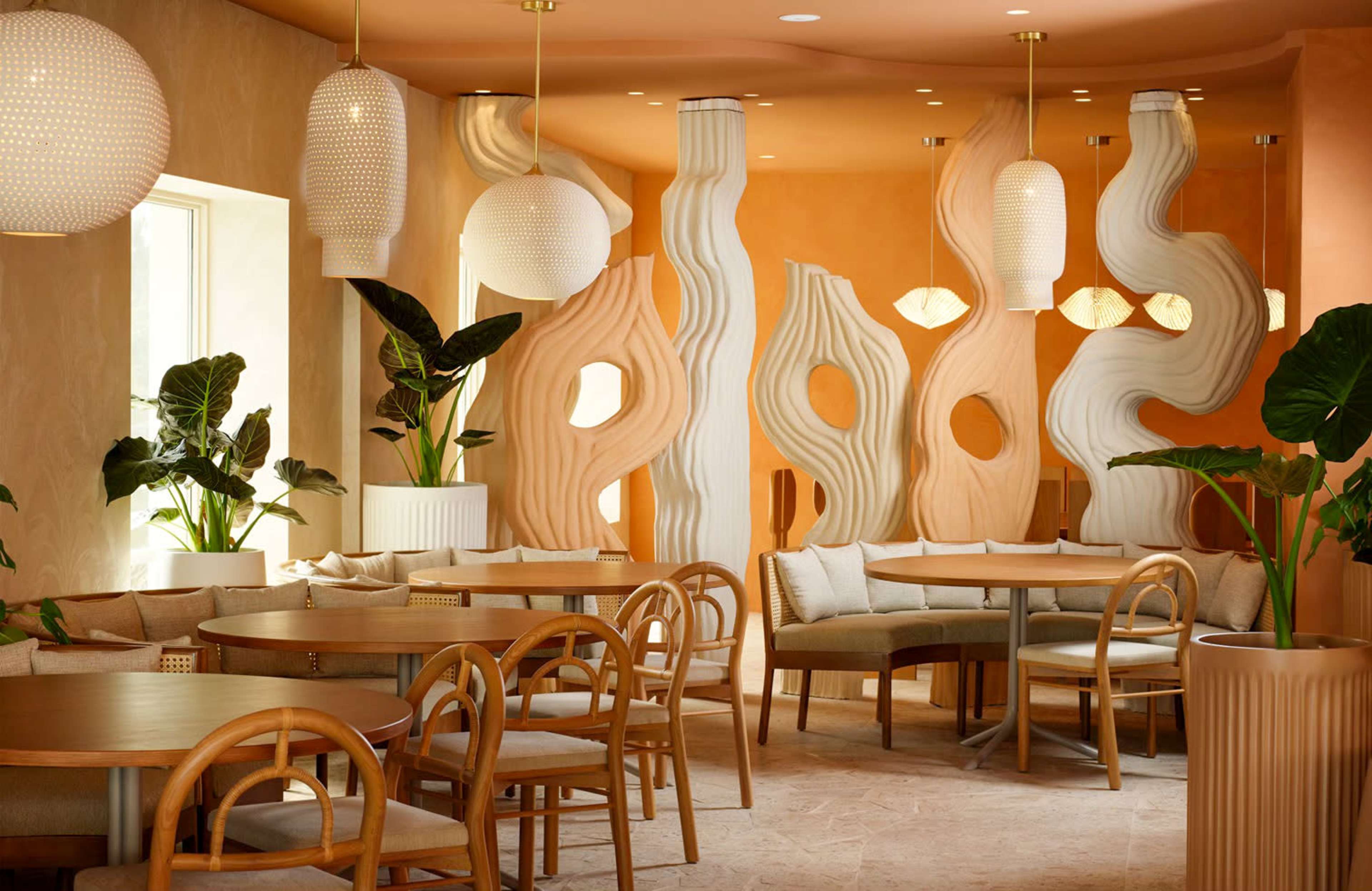 The image shows a stylish café interior with light wood furniture, curved walls, and decorative plants, illuminated by soft pendant lighting.