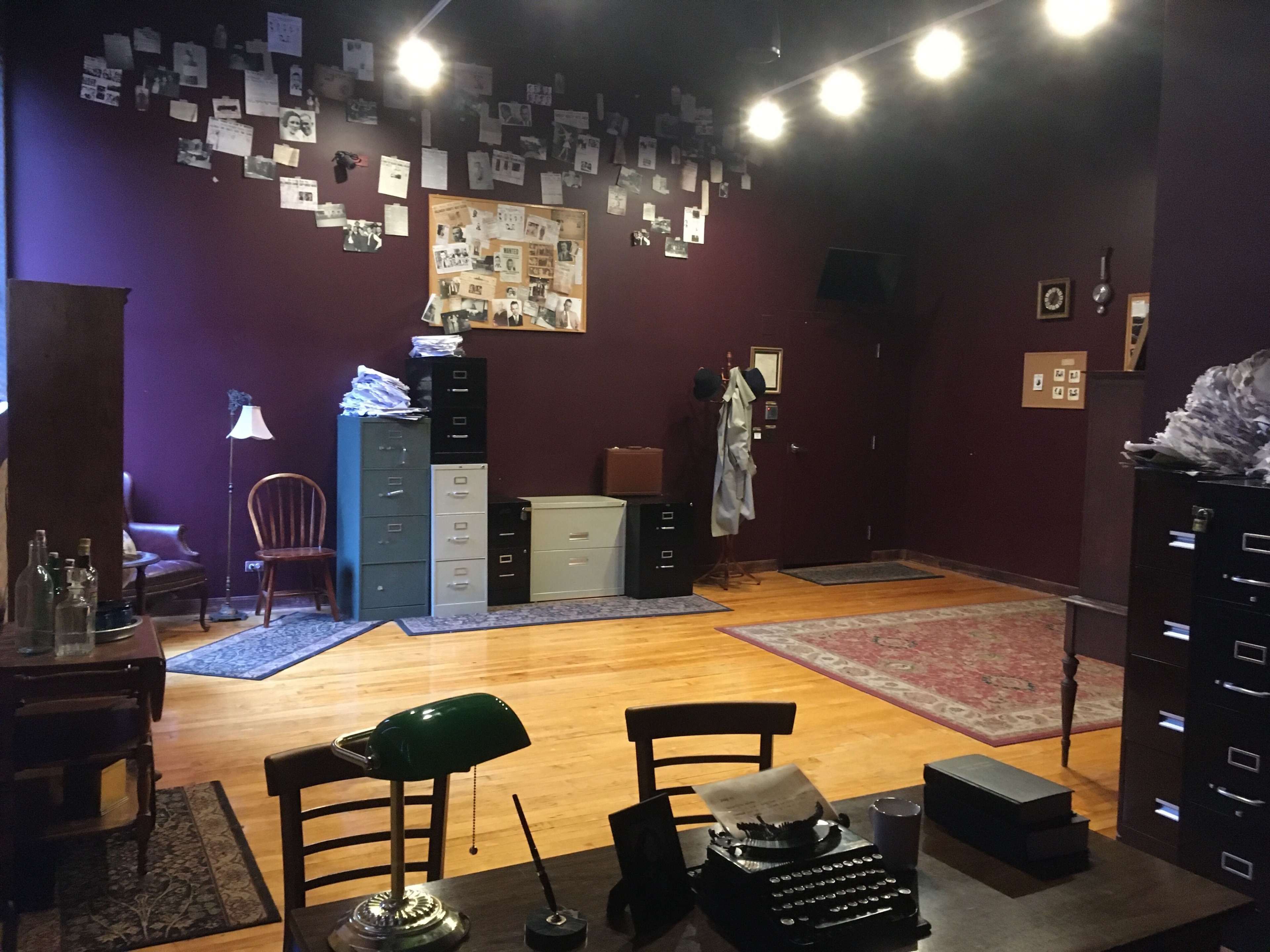 The image shows an office space with purple walls, wooden flooring, a desk with a green lamp and a typewriter, and filing cabinets against the back wall adorned with black-and-white photos.