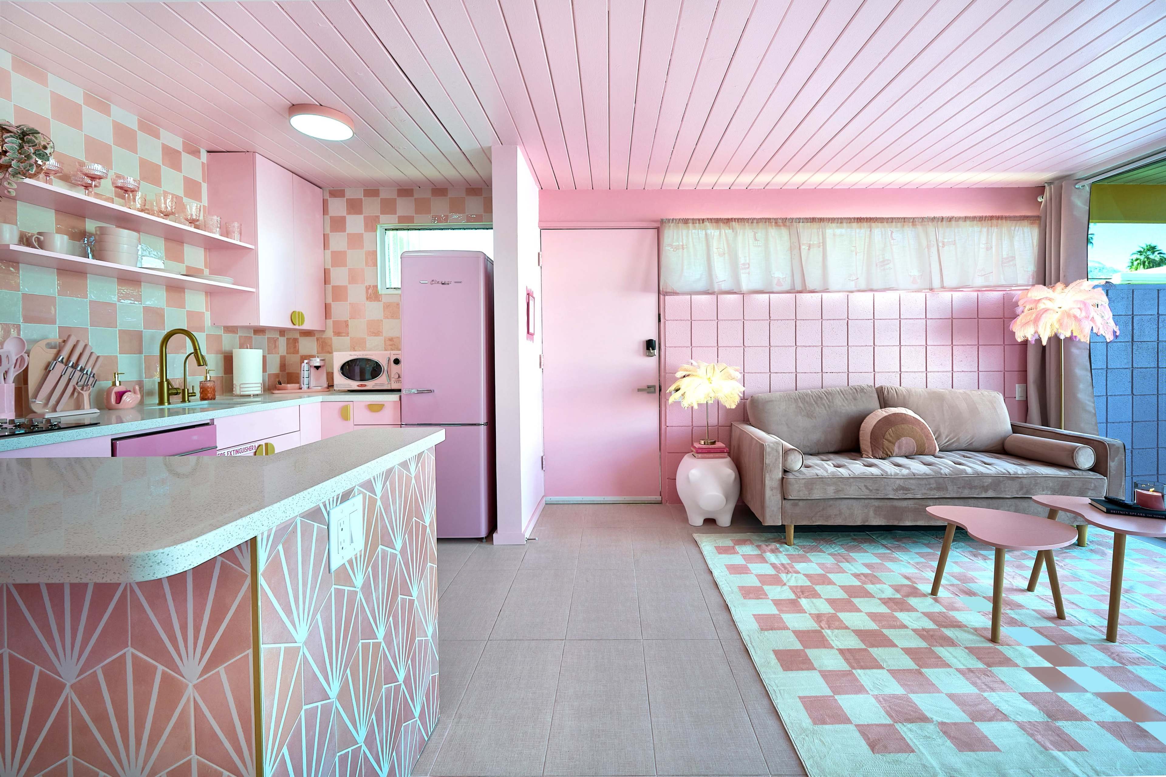 The scene features a brightly colored kitchen and living area, predominantly in shades of pink, with a modern design that includes a sofa, a coffee table, and coordinated decor.