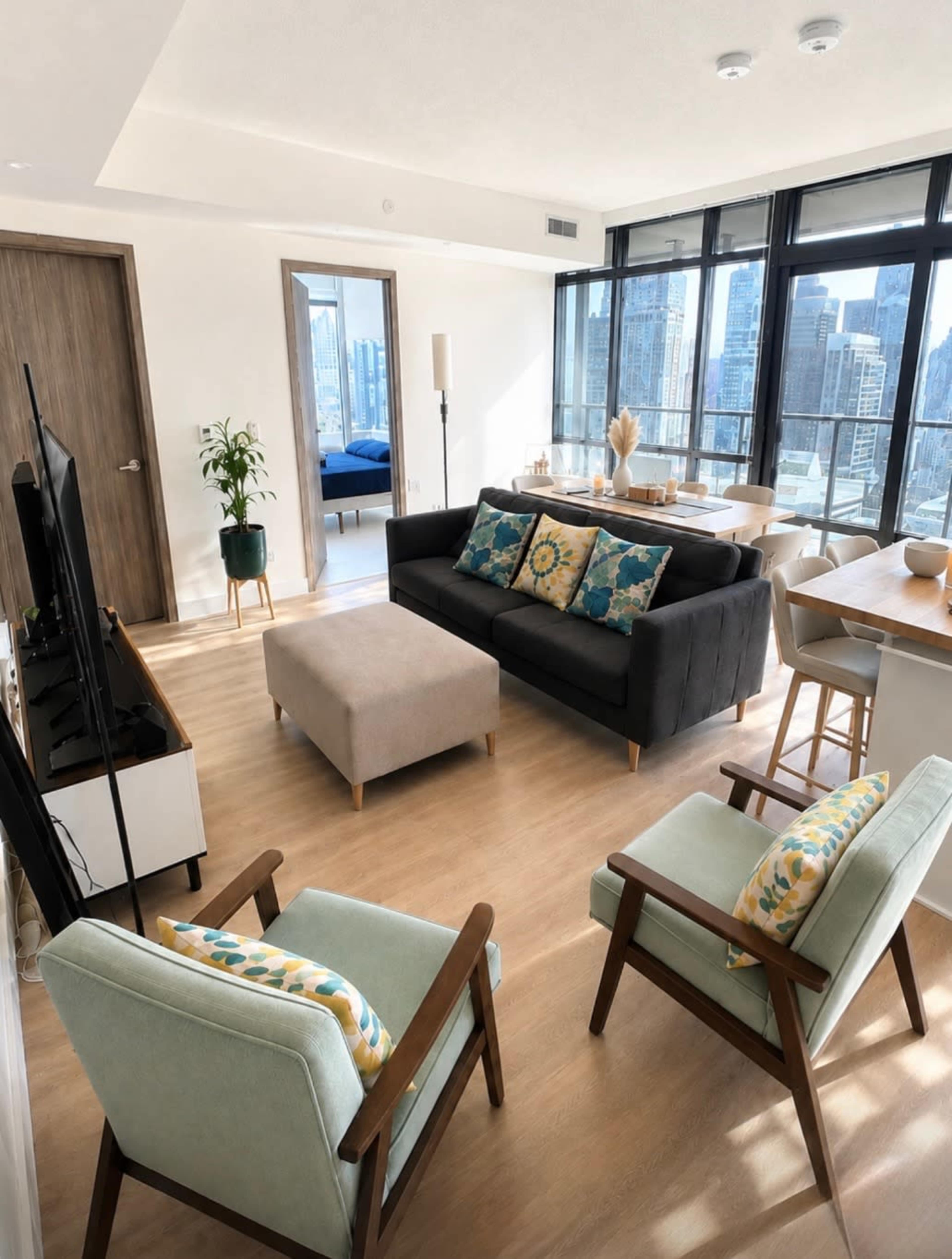 The image shows a modern living room with a gray sofa, two armchairs, a coffee table, and large windows overlooking a city skyline.