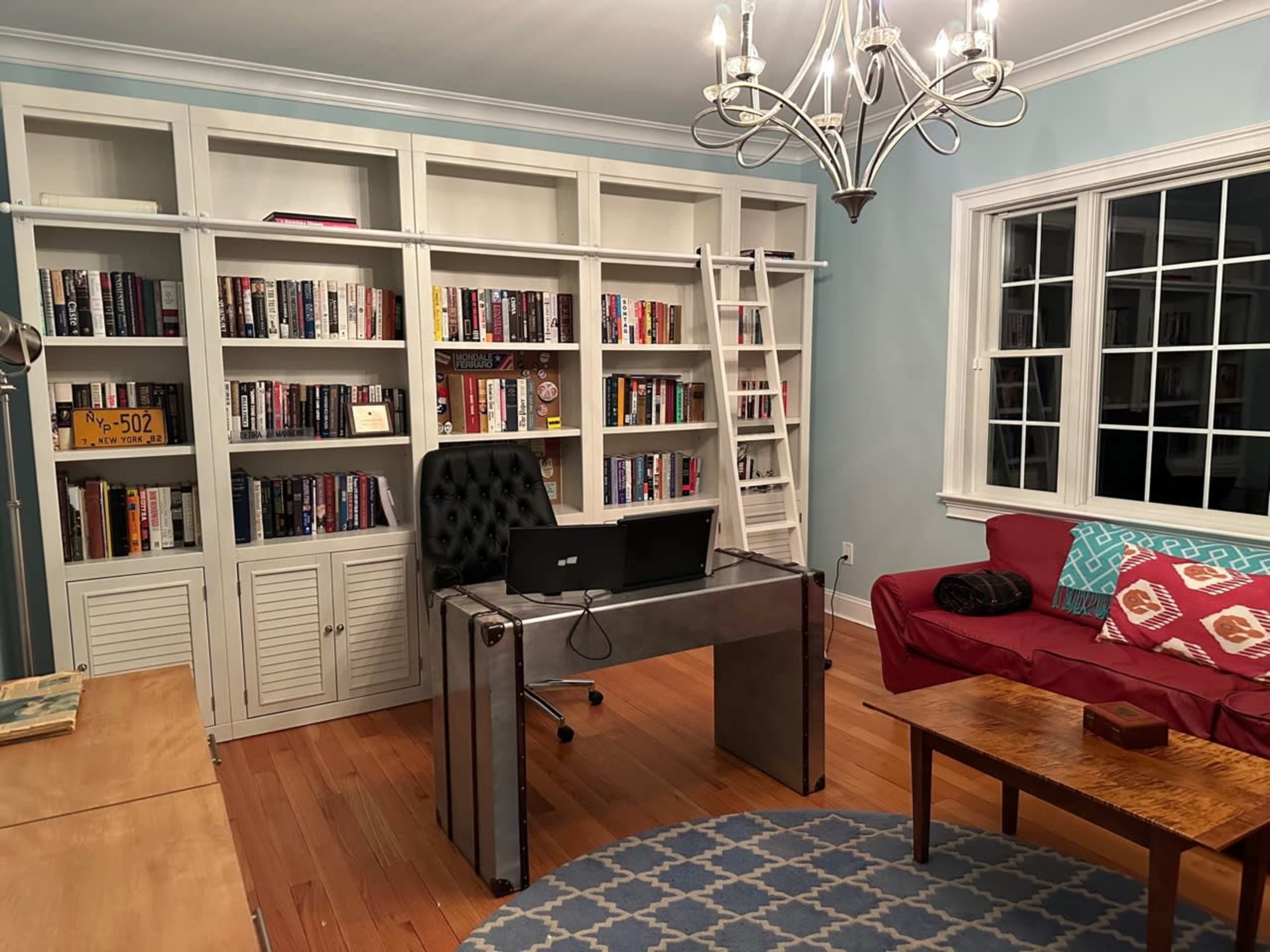 A home office with a metal desk, a computer monitor, a red couch, and a bookshelf filled with books.