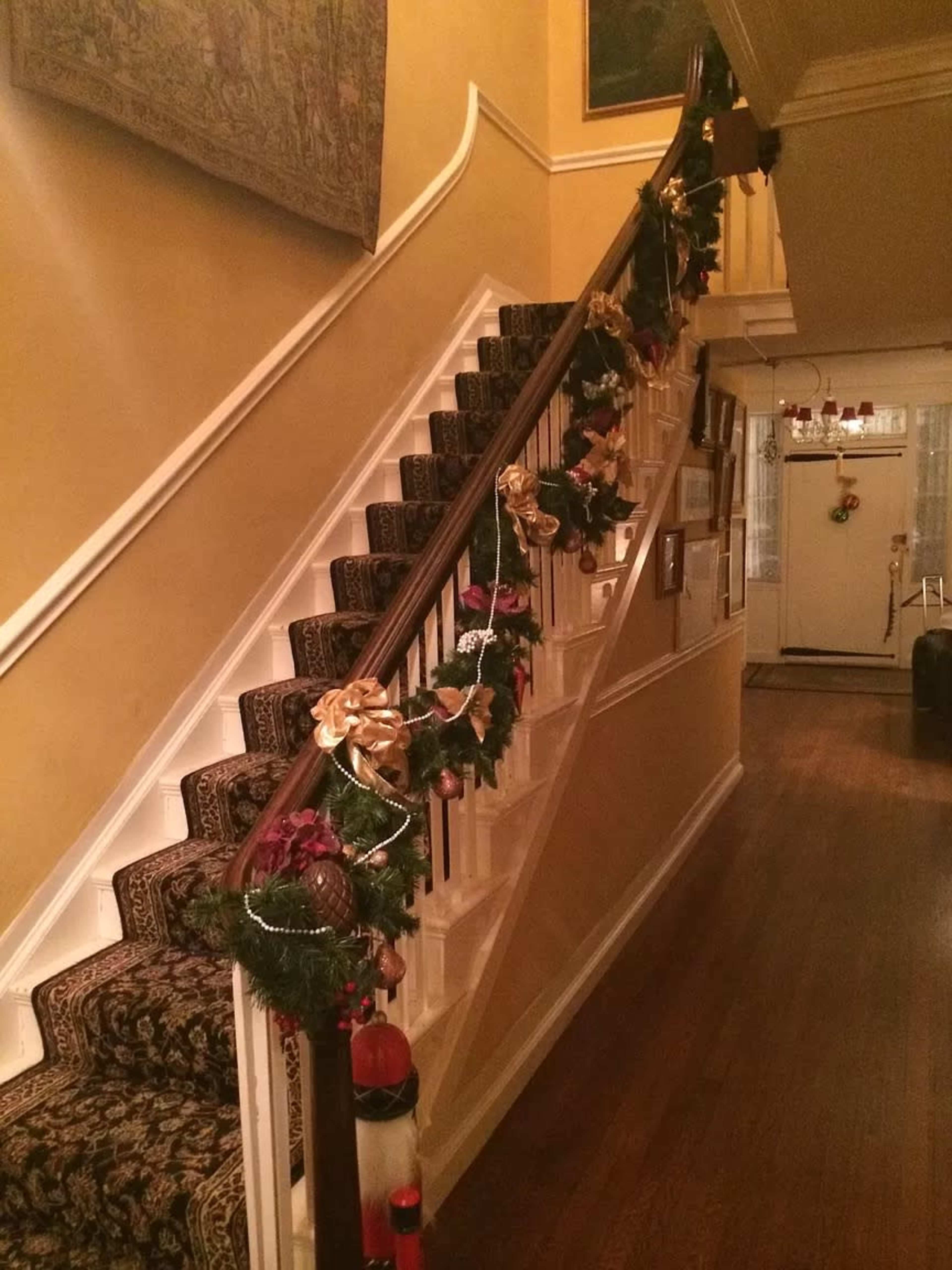 A staircase decorated with garlands, bows, and other festive ornaments, leading up towards a hallway.