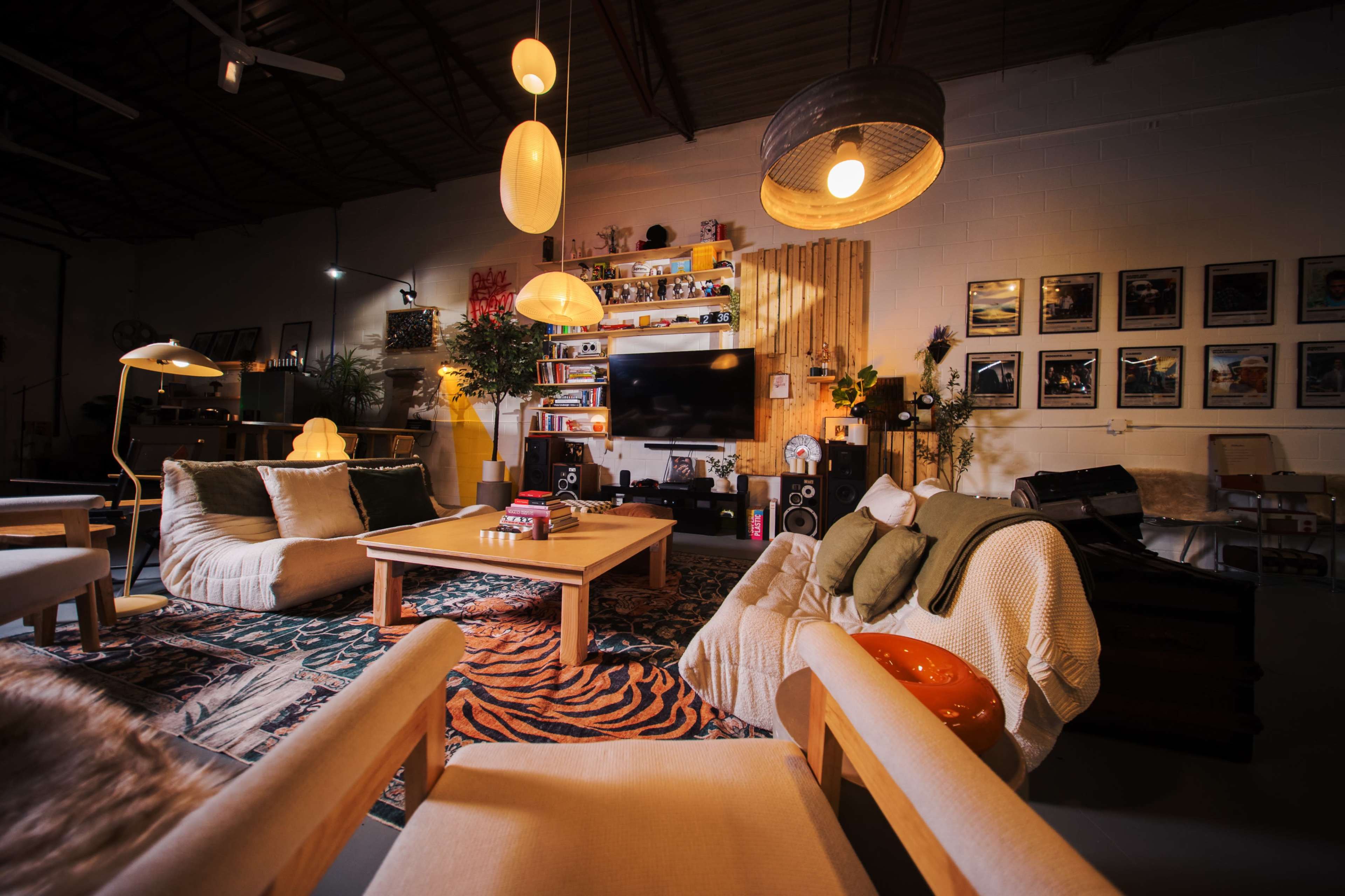 The image shows a cozy living space with modern furniture, a television unit, and decorative plants, all illuminated by various pendant lights.
