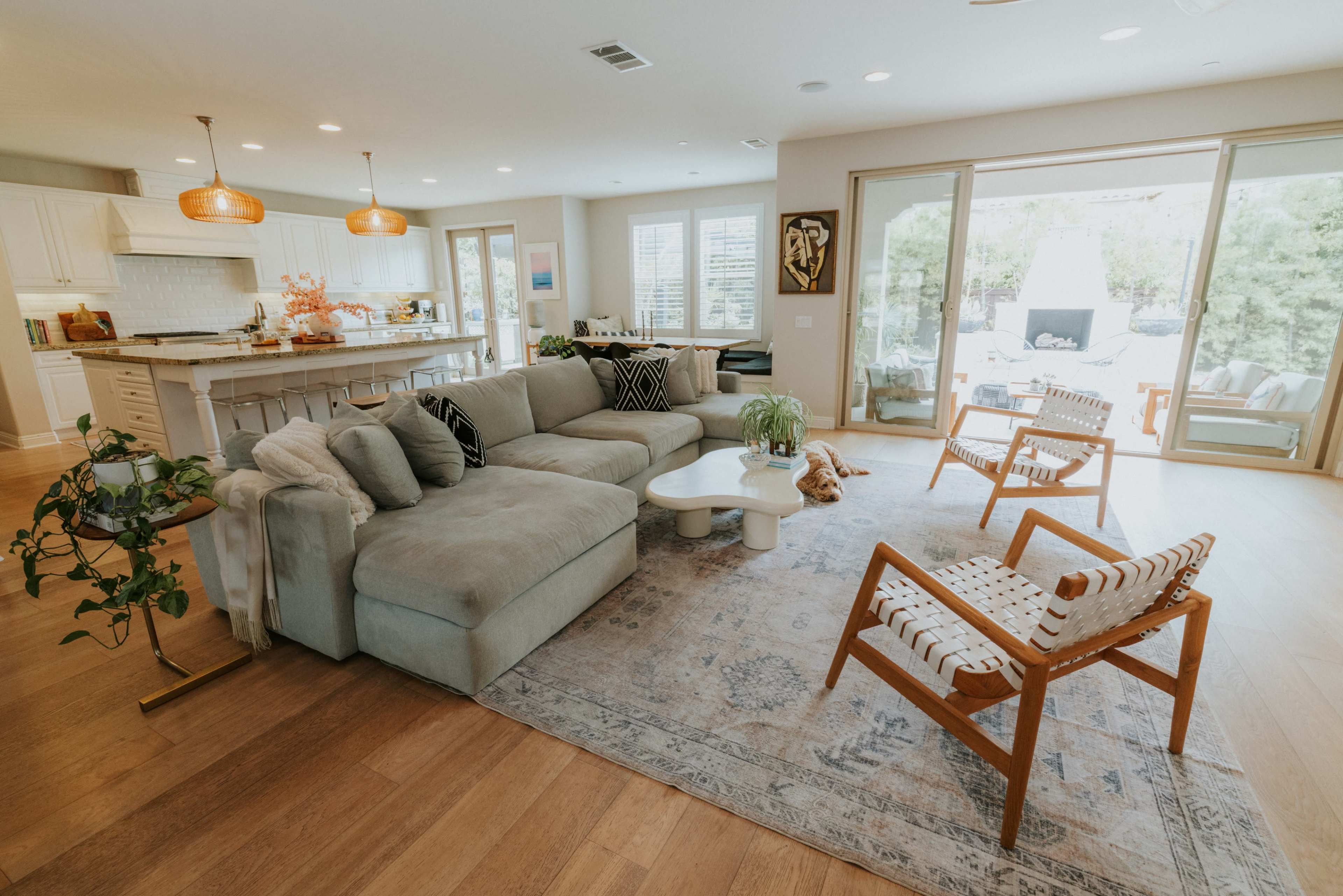 A spacious living room features a large sectional sofa, wooden chairs, a coffee table, and glass doors leading to an outdoor area.