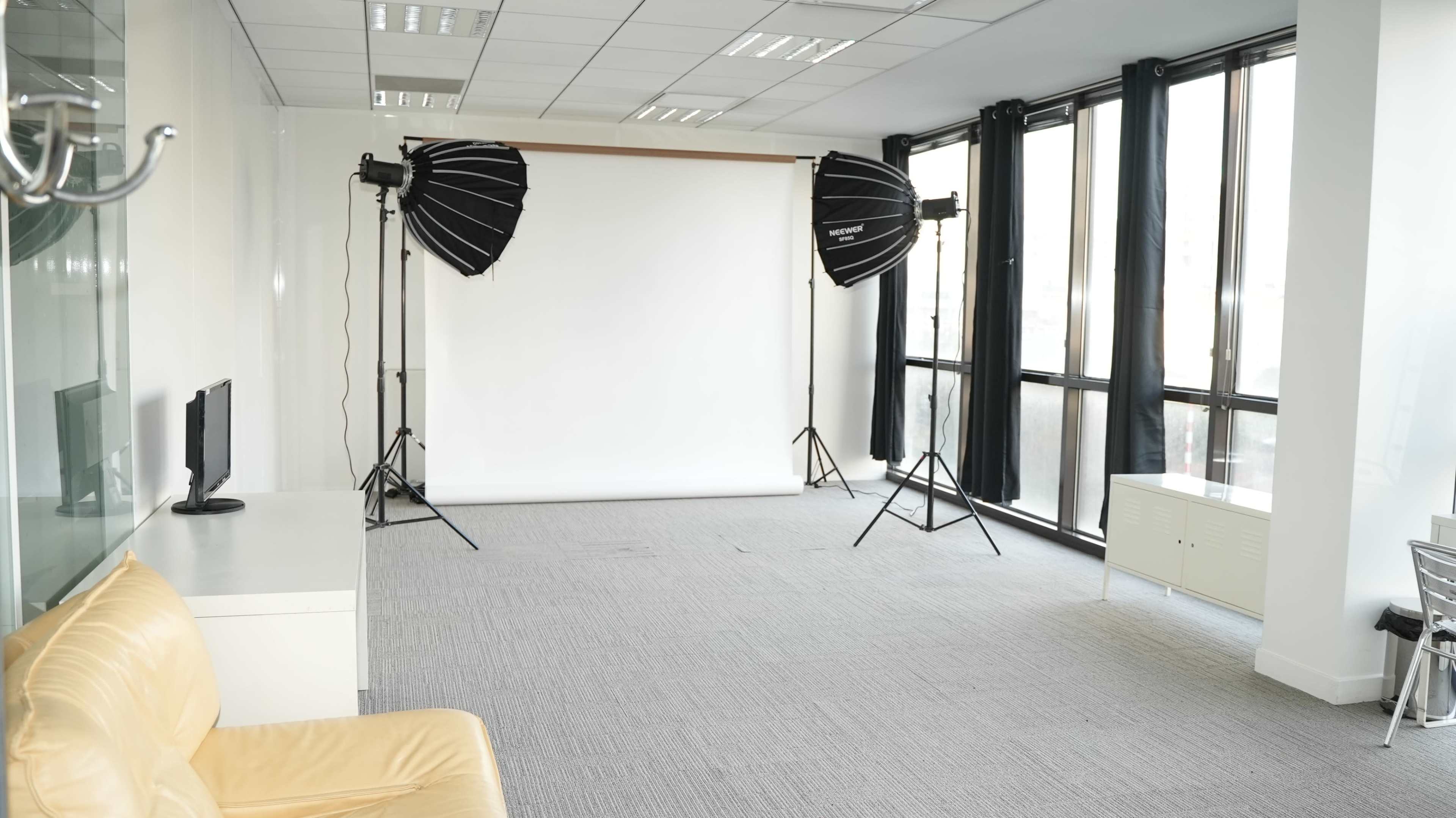 The image shows a spacious, well-lit studio with a plain white backdrop and professional lighting equipment set up in front.