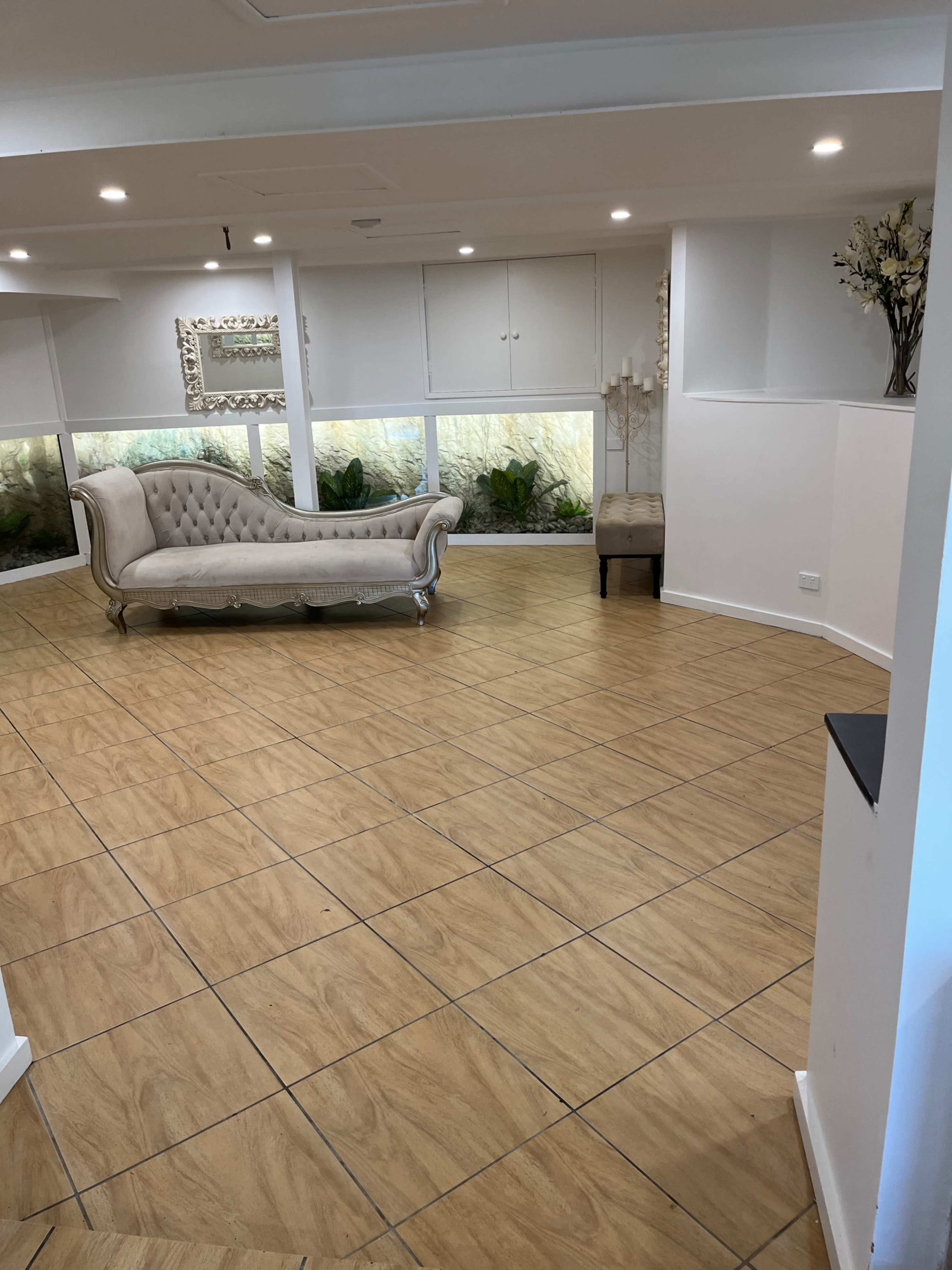The image shows a spacious room with a light-colored, tufted couch, a decorative chair, and large windows allowing natural light inside.