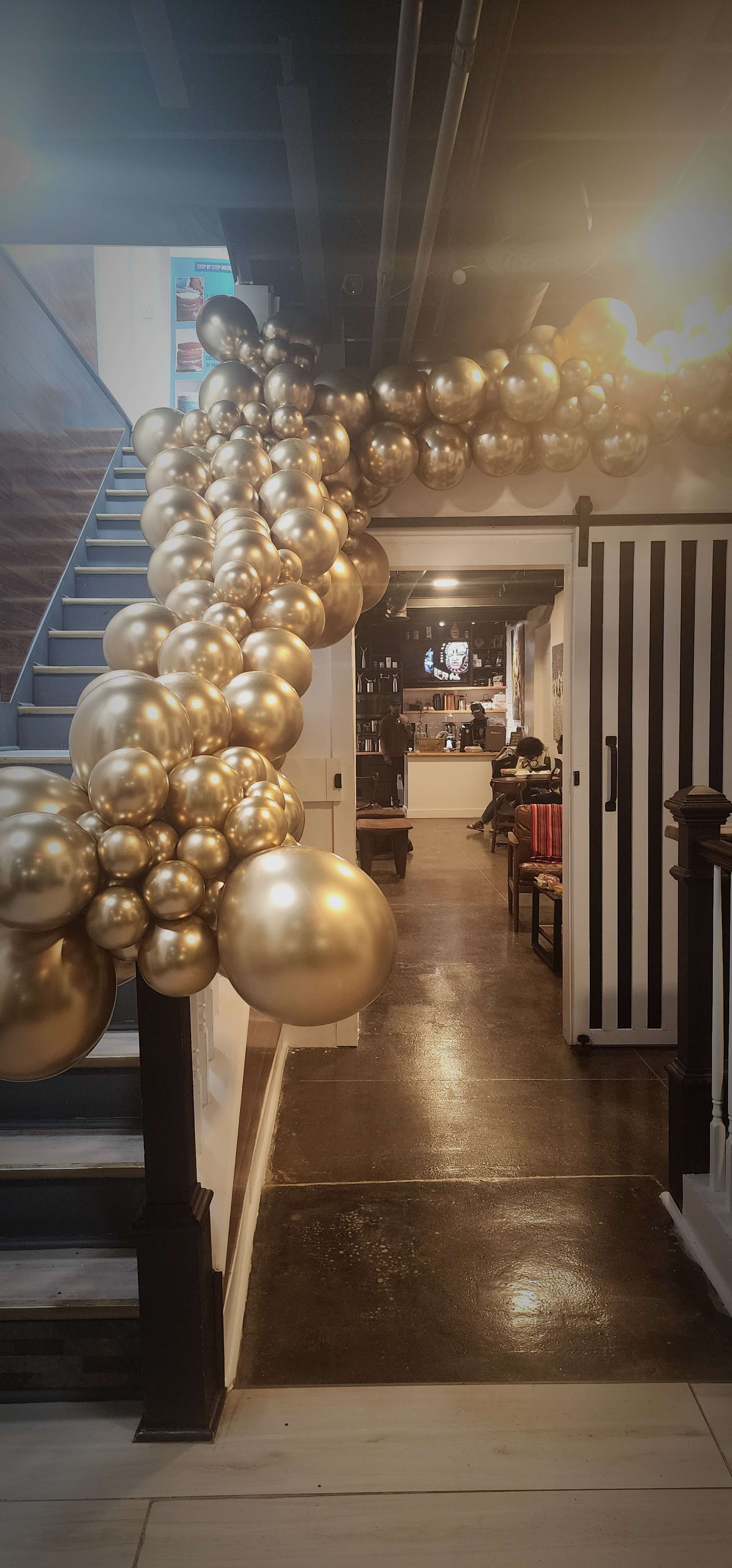 A decorative arrangement of golden balloons winds along a staircase leading to a dining area.