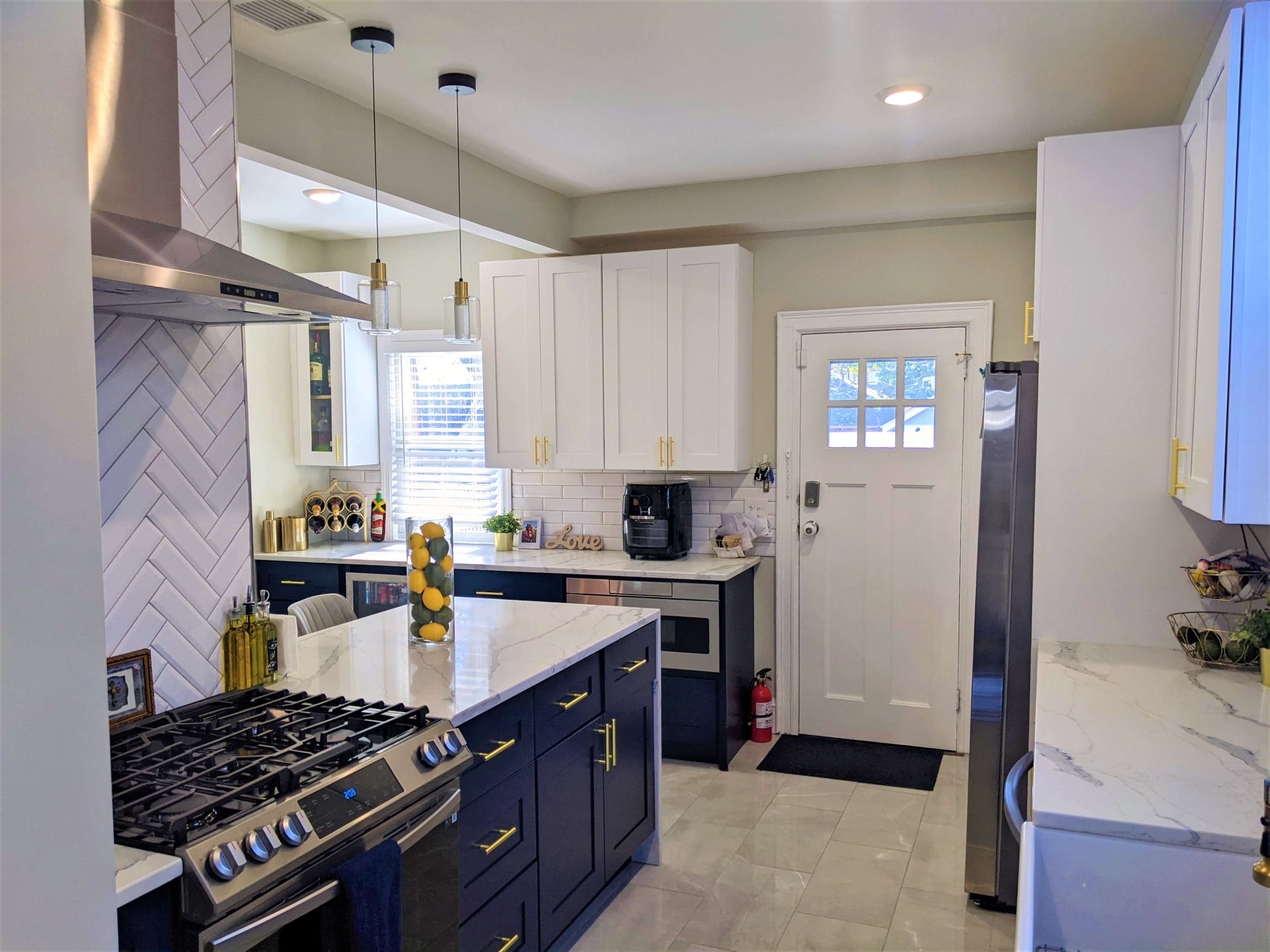 A modern kitchen featuring a marble island, dark blue cabinetry, stainless steel appliances, and a door leading outside.