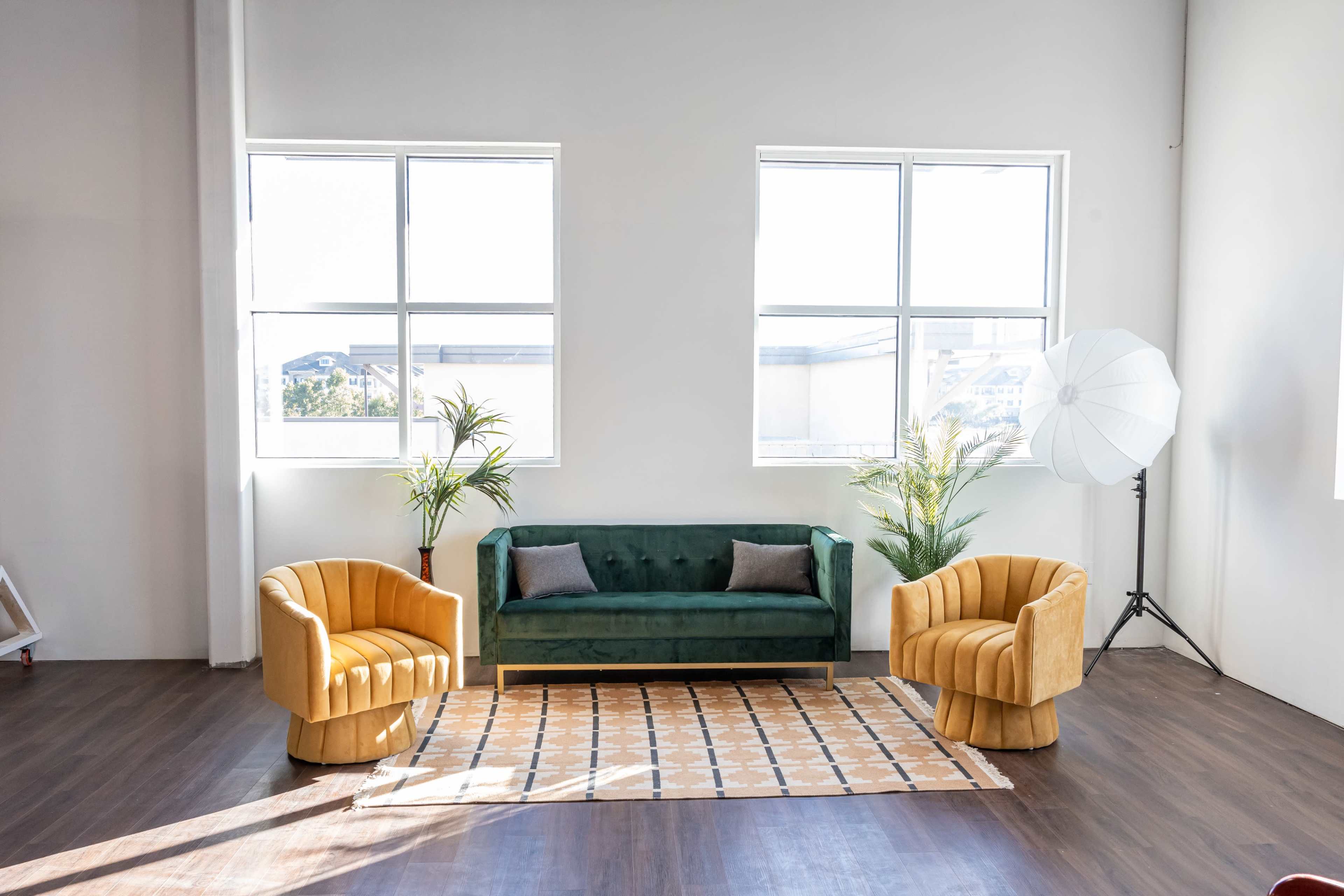 The image shows a spacious room with a green sofa, two yellow accent chairs, and large windows that allow natural light to fill the space.