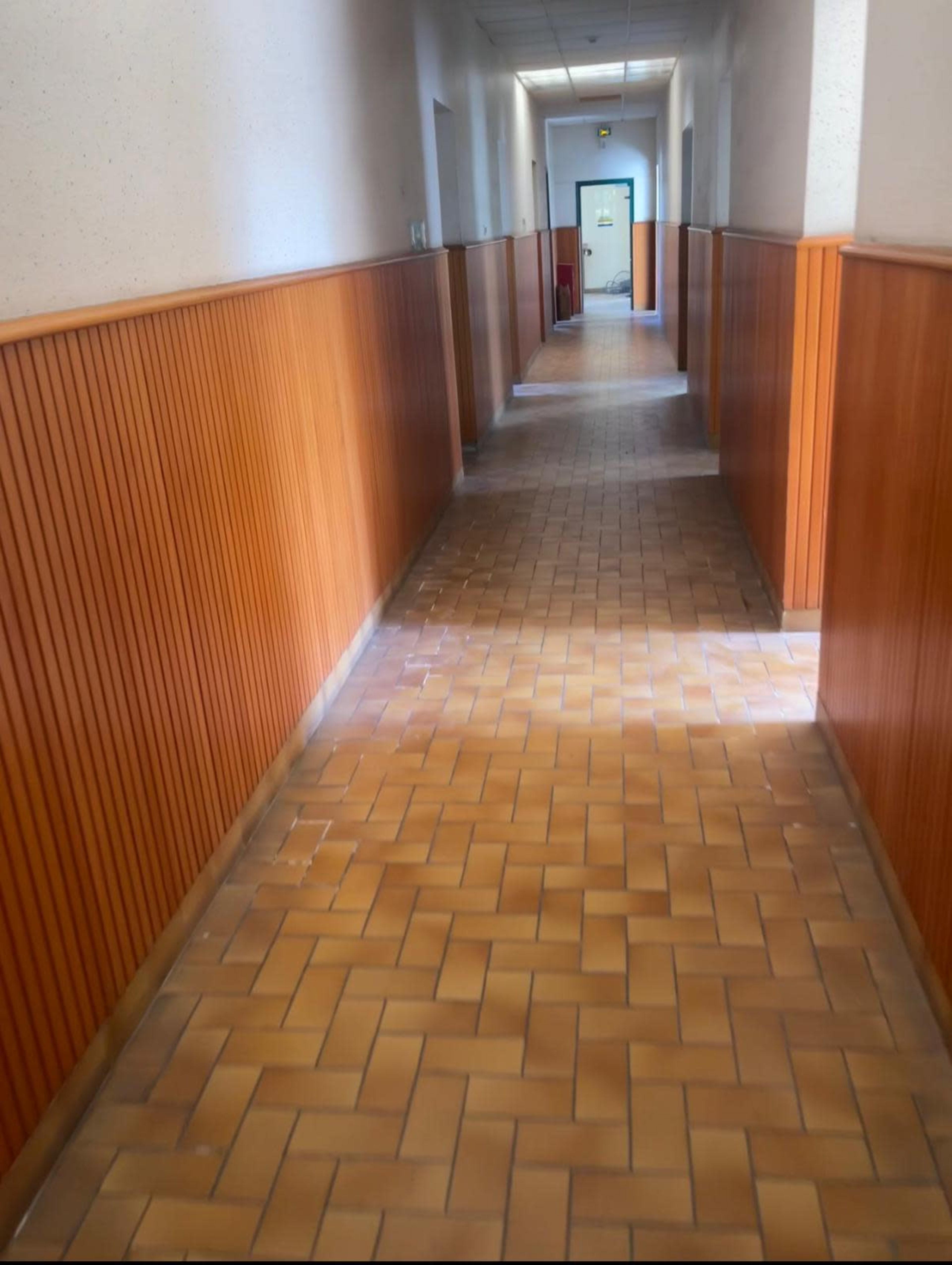 A long hallway with wooden paneling and tile flooring leads to a door at the far end.