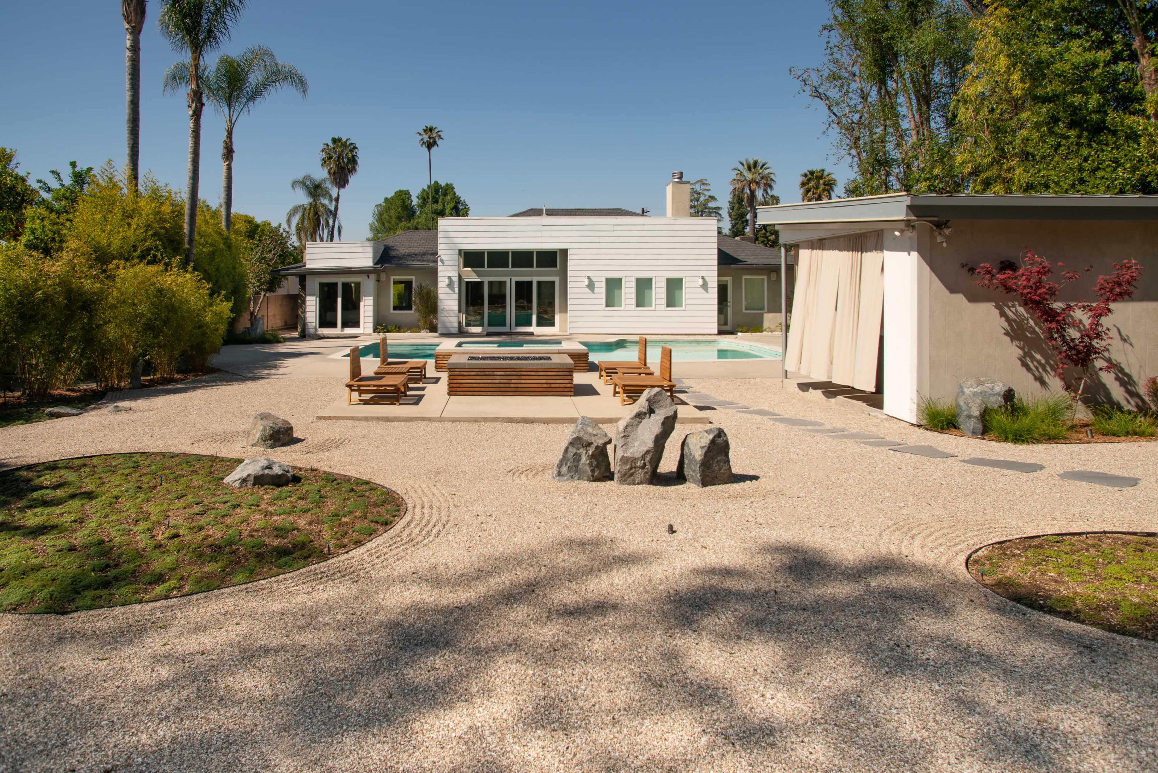 A modern house with a pool surrounded by a landscaped yard featuring gravel pathways, wooden decks, and decorative rocks.
