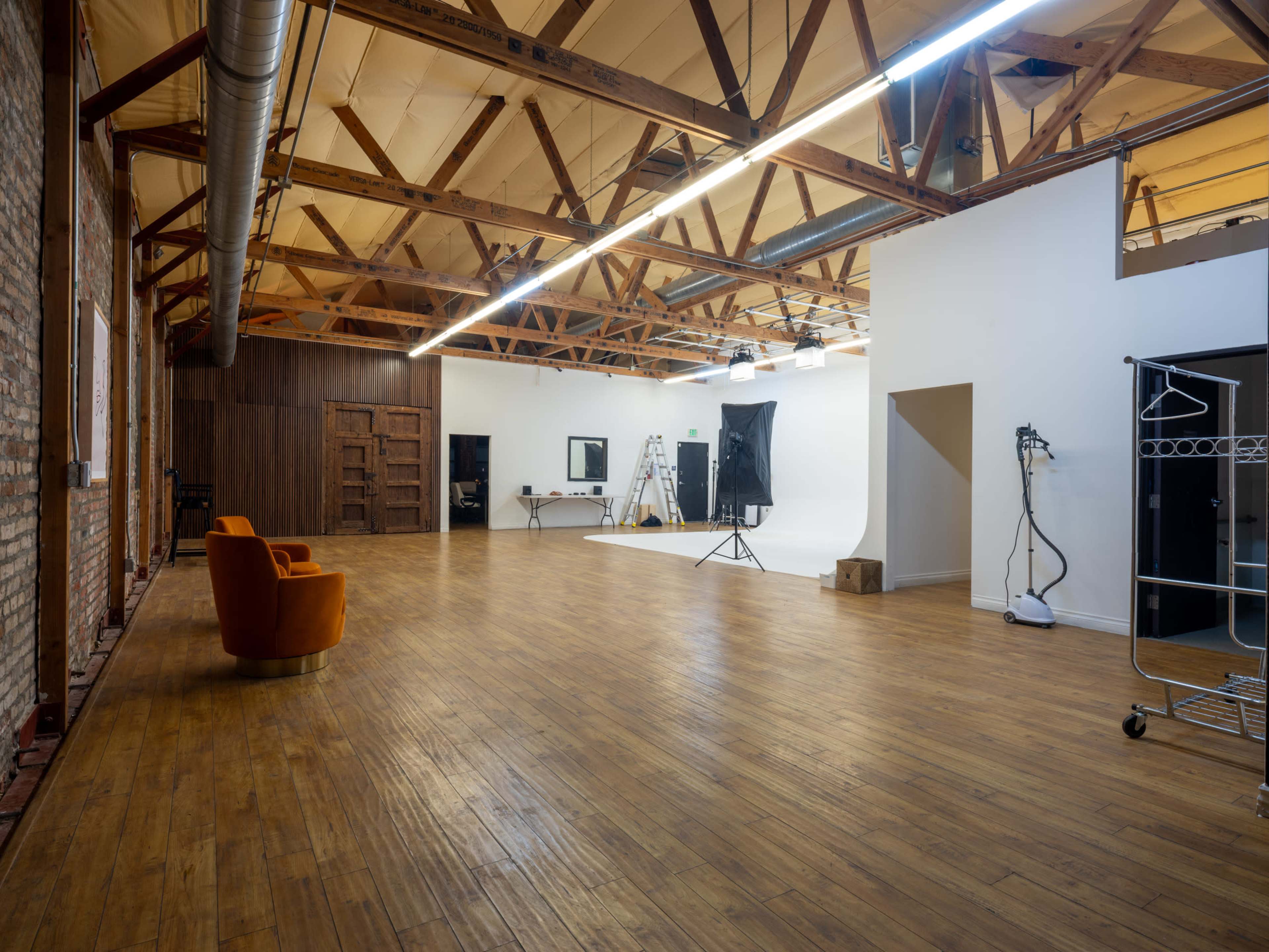 The image shows a spacious, well-lit photography studio with wooden floors, exposed beams, and various equipment set up for a photoshoot.