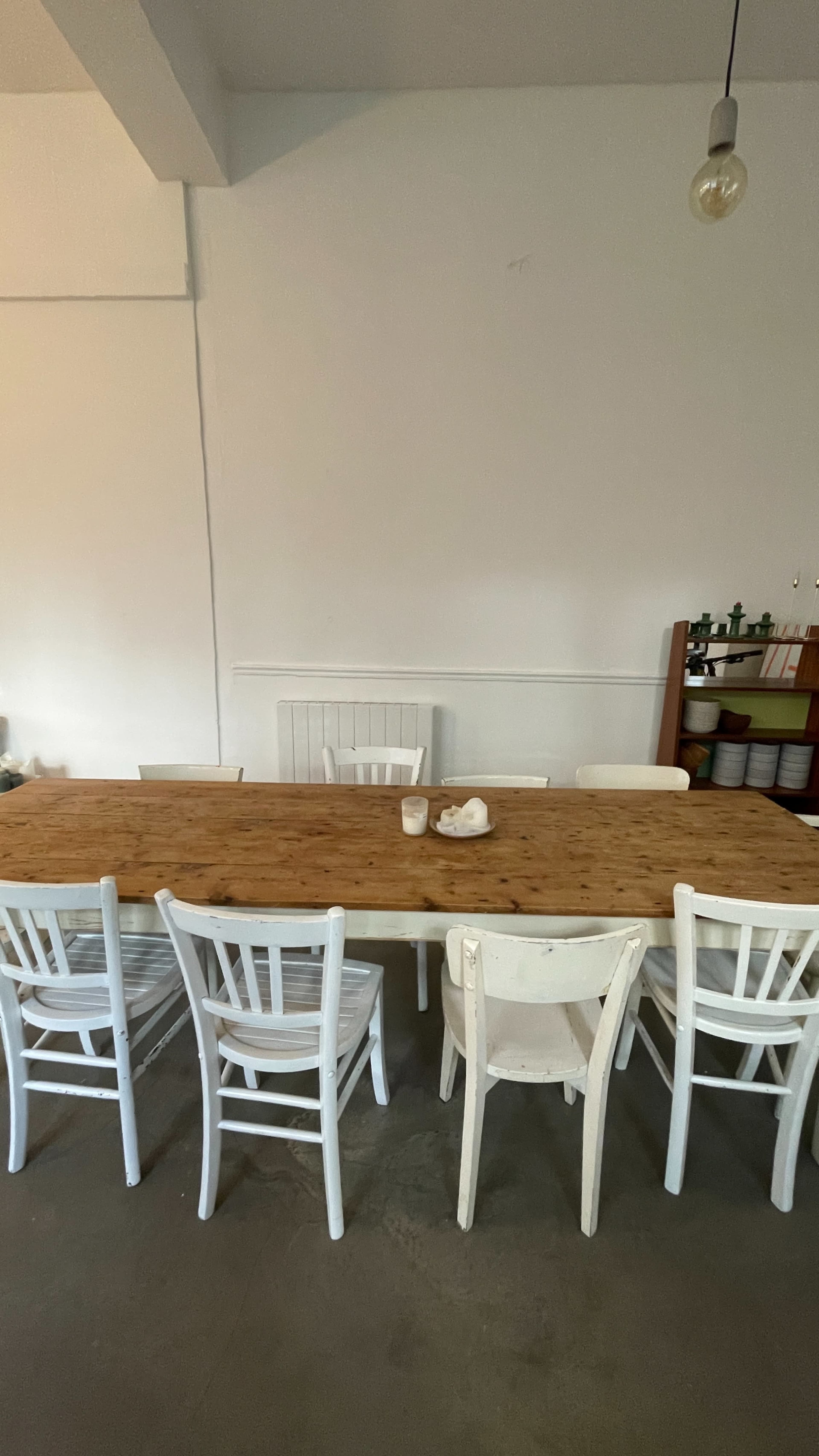 A long wooden table with several white chairs surrounds it in a simple, minimalist dining area.